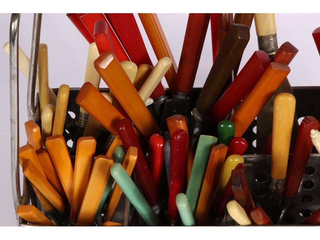A colorful large collection of vintage cutlery having red, green, amber, black, brown, ivory and tortoise color handles. The collection is held in a handled and pierced vintage chrome commercial restaurant caddy. A great group for the Mid-Century or