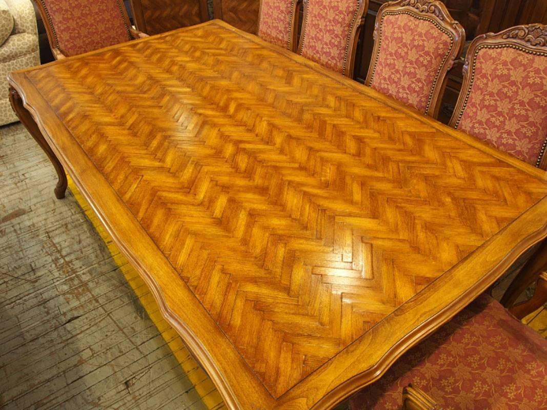 A solid dining table with coordinating chairs. Nicely carved wood with floral crests, apron and legs. Intricate parquetry work to table top. Upholstery on chairs is in very good condition in a cranberry with cream maple leaf pattern. Brass tack trim
