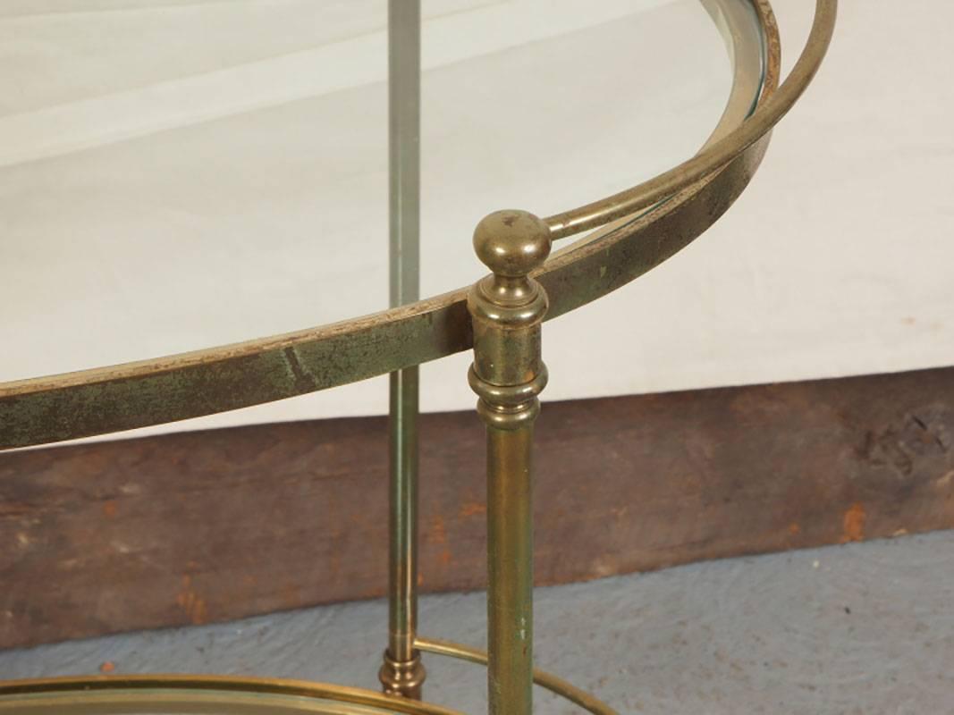 Two-tier oval brass and glass bar cart with conforming brass gallery and raised up on casters.
Condition: Brass has wear and oxidation consistent with age; glass with minor light scratches.