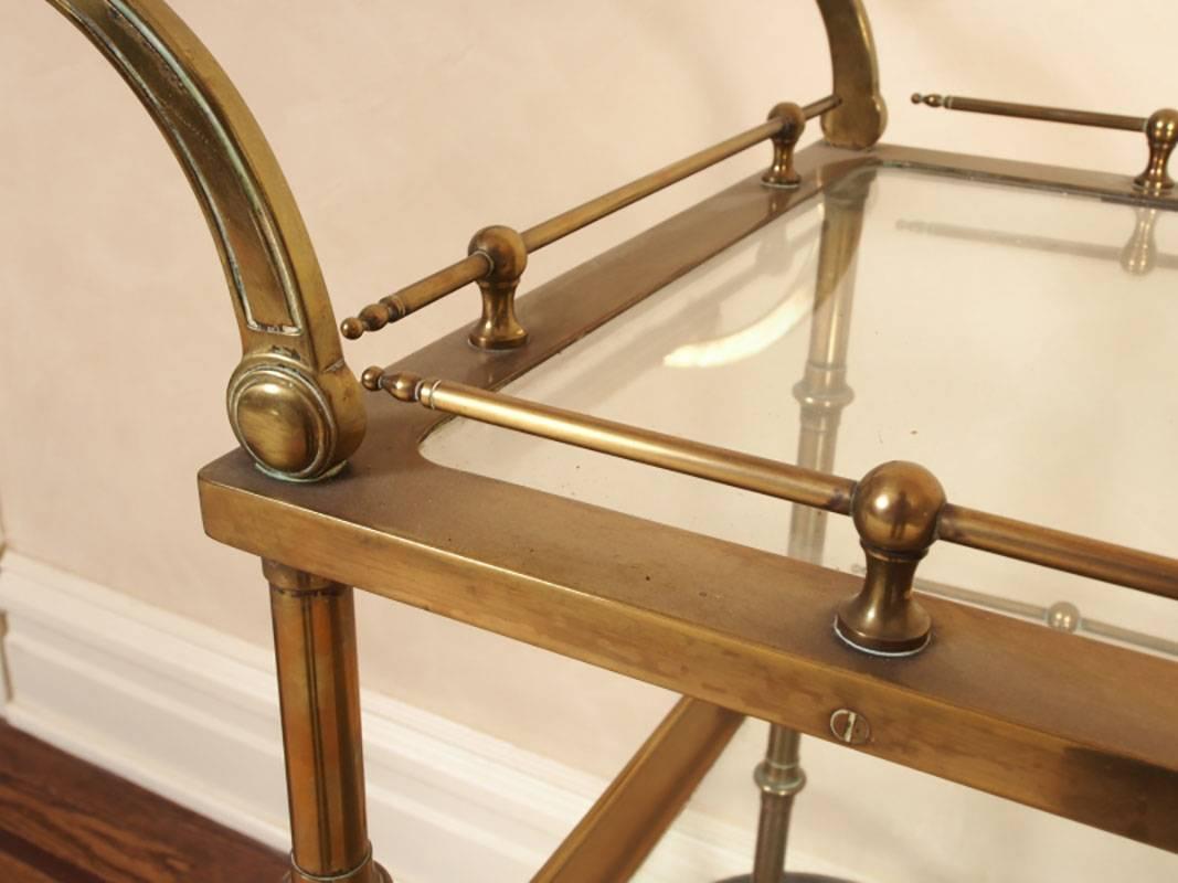 Heavy brass and glass bar cart with castered front feet and spoke wheel back wheels, brass galleries, glass shelves.
Condition: Age appropriate wear including light scratches to glass, oxidation to brass consistent with age.