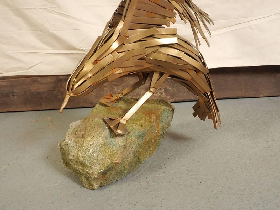 Iron in gold paint. The entire bird formed of thin rectangular pieces of painted iron of various sizes. The eagle has just landed with spread wings, tail and talons on a rough block of stone in green paint. 
Base measures 24