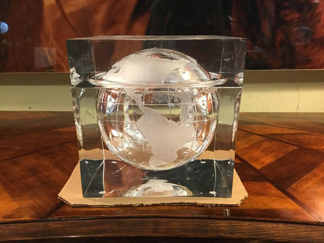 Heavy, Lucite ice bucket in the form of a world globe suspended in a cube. The interior is embossed with earth having longitude and latitude lines. The moon is included in the rim of lid and base.
Condition: Some sporadic crackling in the Lucite,