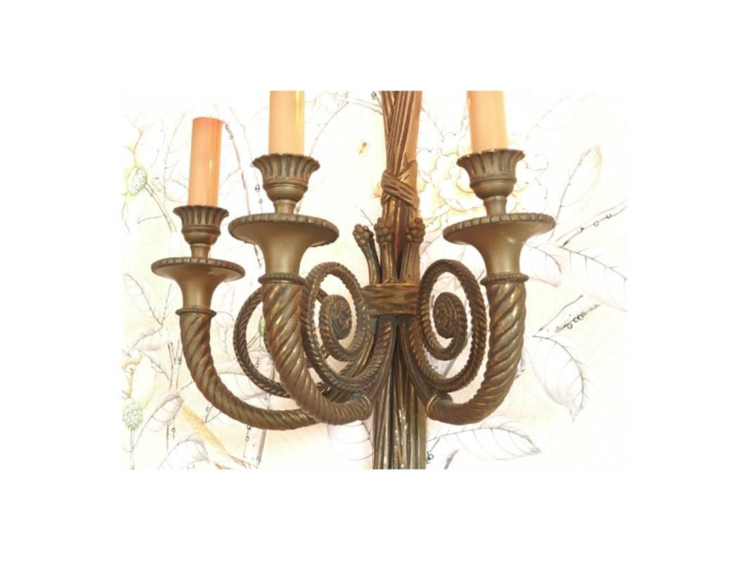 Pair of bronze wall sconces with tied loop ending in tassels holding three twisted and fluted arms. 
Condition: One with slight scratches to lower portion, otherwise consistent with age.