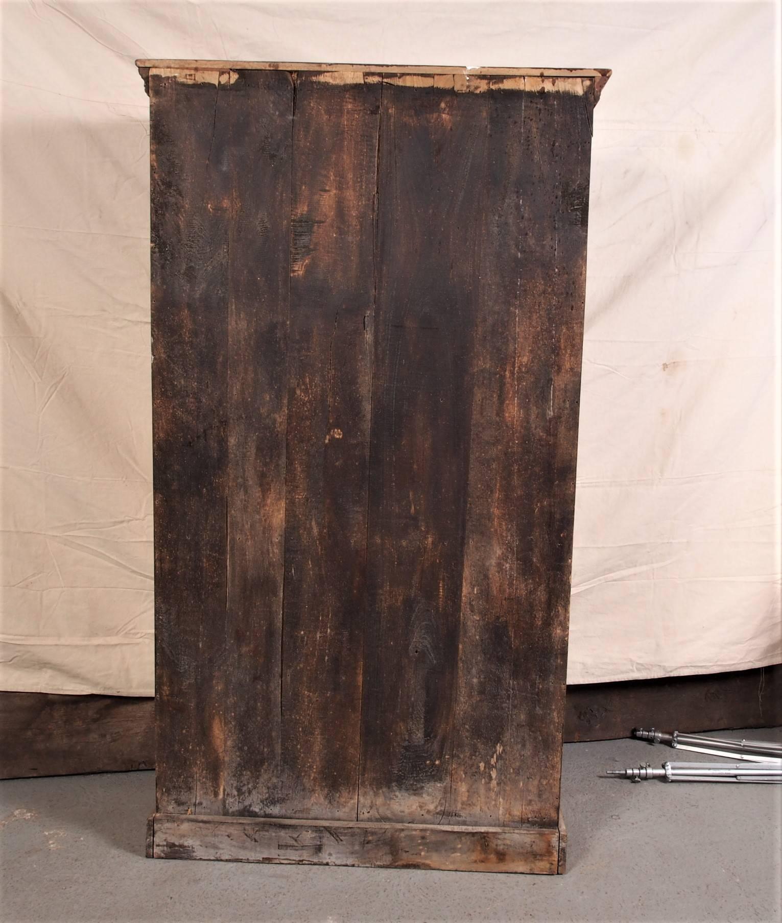 Antique four shelf bookcase cabinet with carved floral panel, planked construction, crown molding and raised on a plinth base.
Condition: distressed, consistent with age and use.