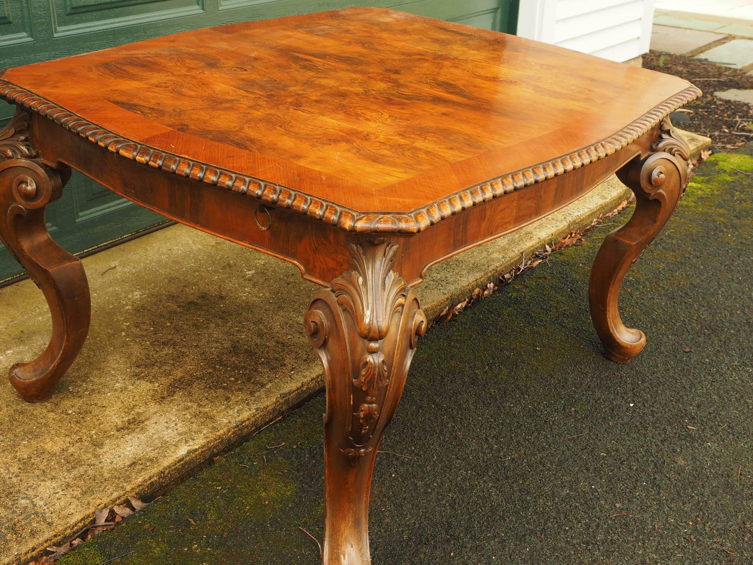 With a shaped top of figured walnut with mahogany crossbanding, carved gadrooned border, and canted corners. A figured walnut apron with one ring preserved, the whole raised on heavily carved cabriole legs with scrolled acanthus leaf knees.