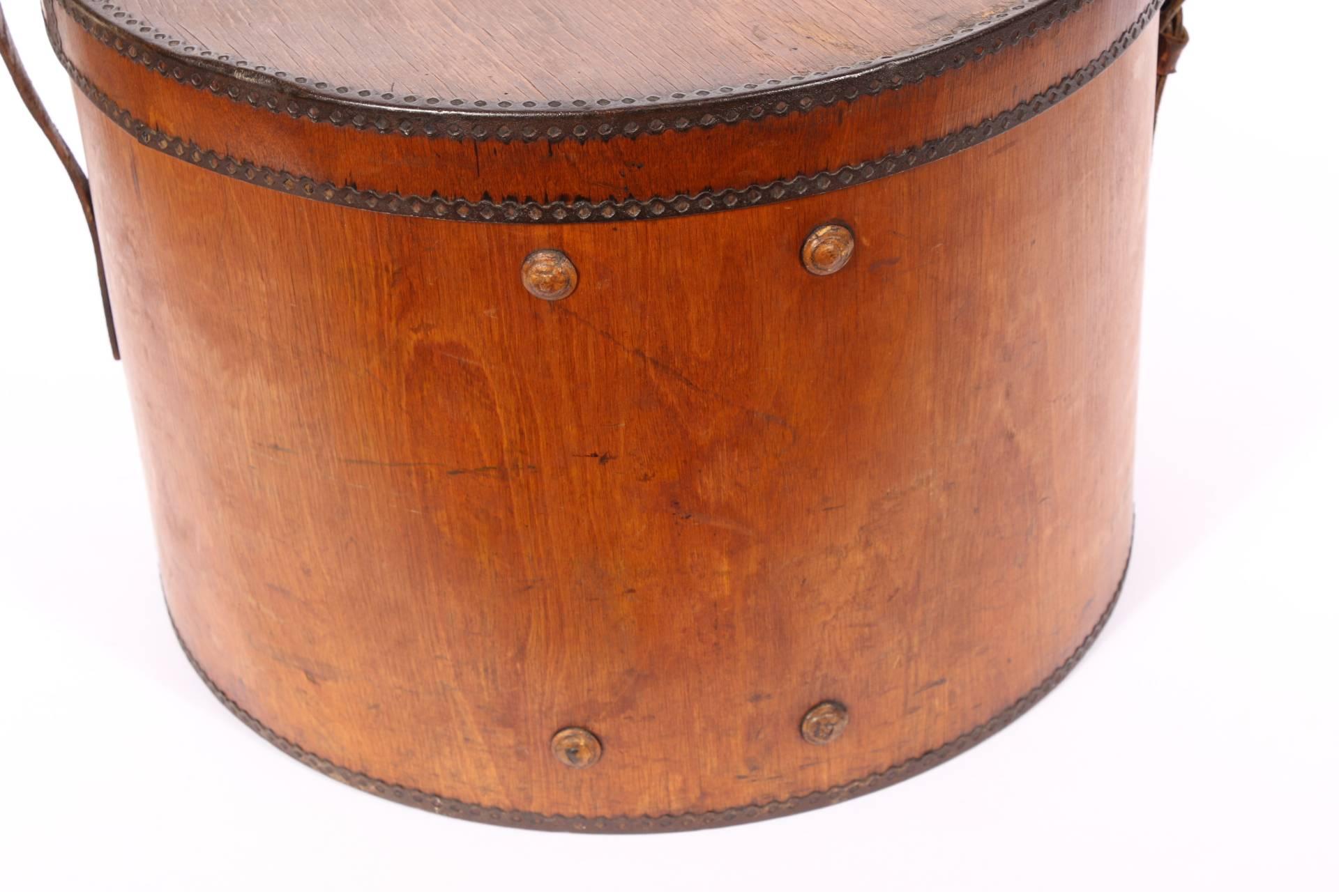19th century wooden hat box having a circular form with leather strap and handle, crimped metal frame, wood button decorated.
Condition: some alligatoring to wood, wear to leather, consistent with age and use.