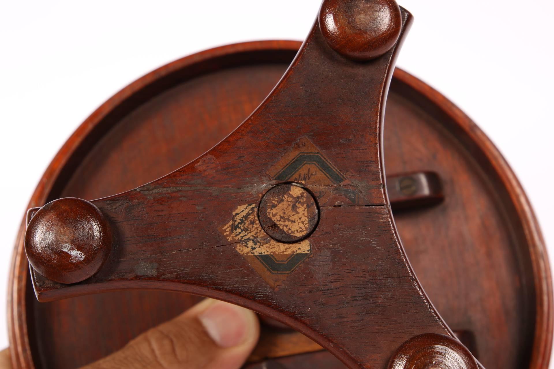 Mahogany and satinwood with a starburst patterned top, carved top edge, and a turned and reeded support on a tripod base with bun feet. With a wooden hinge on the bottom for the tilt mechanism. Old paper label on the bottom.
In fine condition with