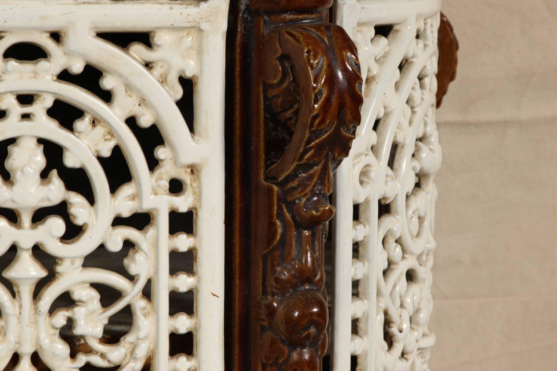 Shaped oval form with neoclassical decoration in brown and white enamel. Four openwork doors and top with medallions of putti warming their hands at fires, acanthus leaves on the supports and scrolled feet. Silver plate pulls. A tin back pierced