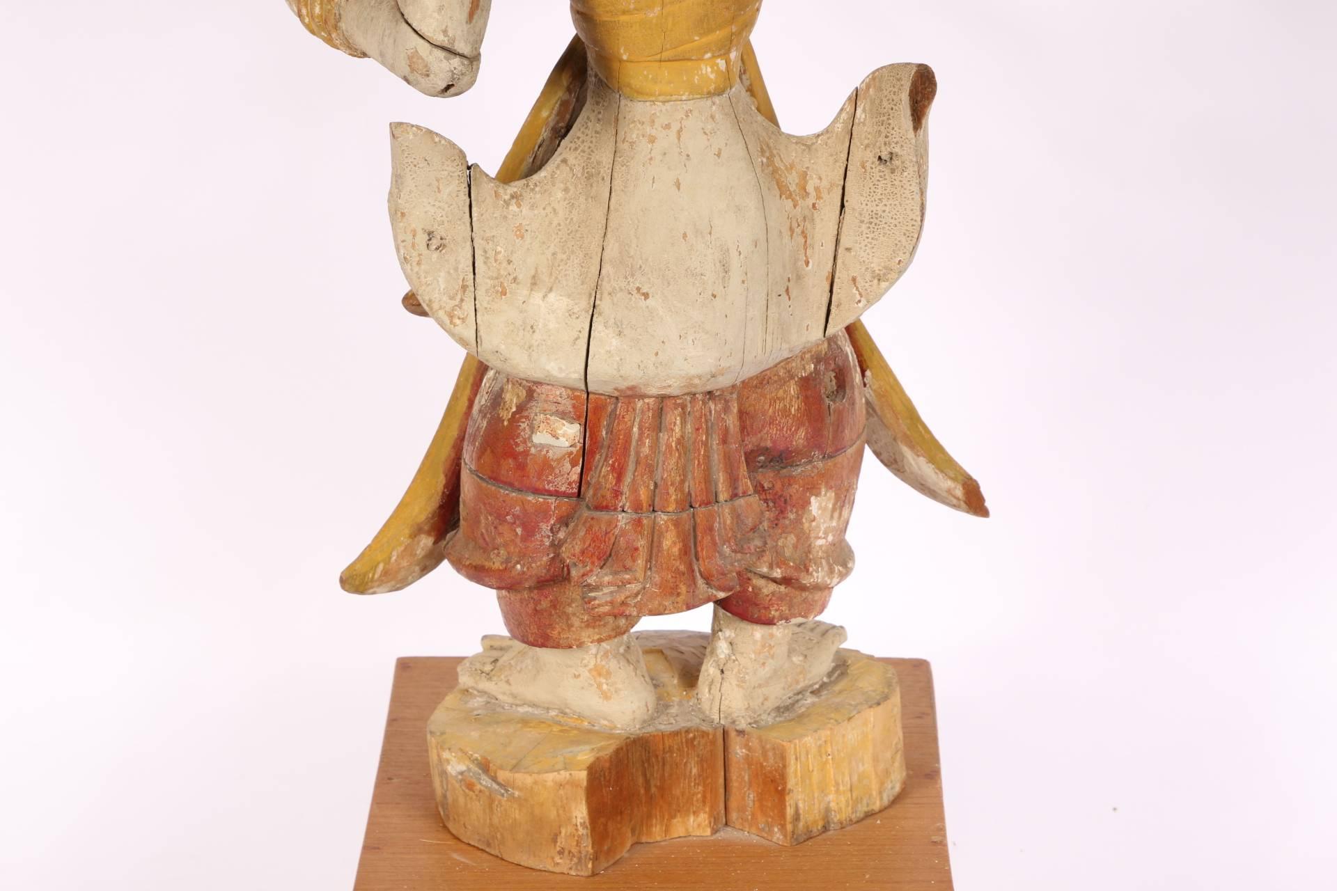 Carved and painted wood made in numerous sections. A court dancer in an elegant pose painted cream wearing a cream and yellow skirt, red tied trousers, yellow sash, tall yellow headdress and bracelets. On a carved oval painted base with a notch on
