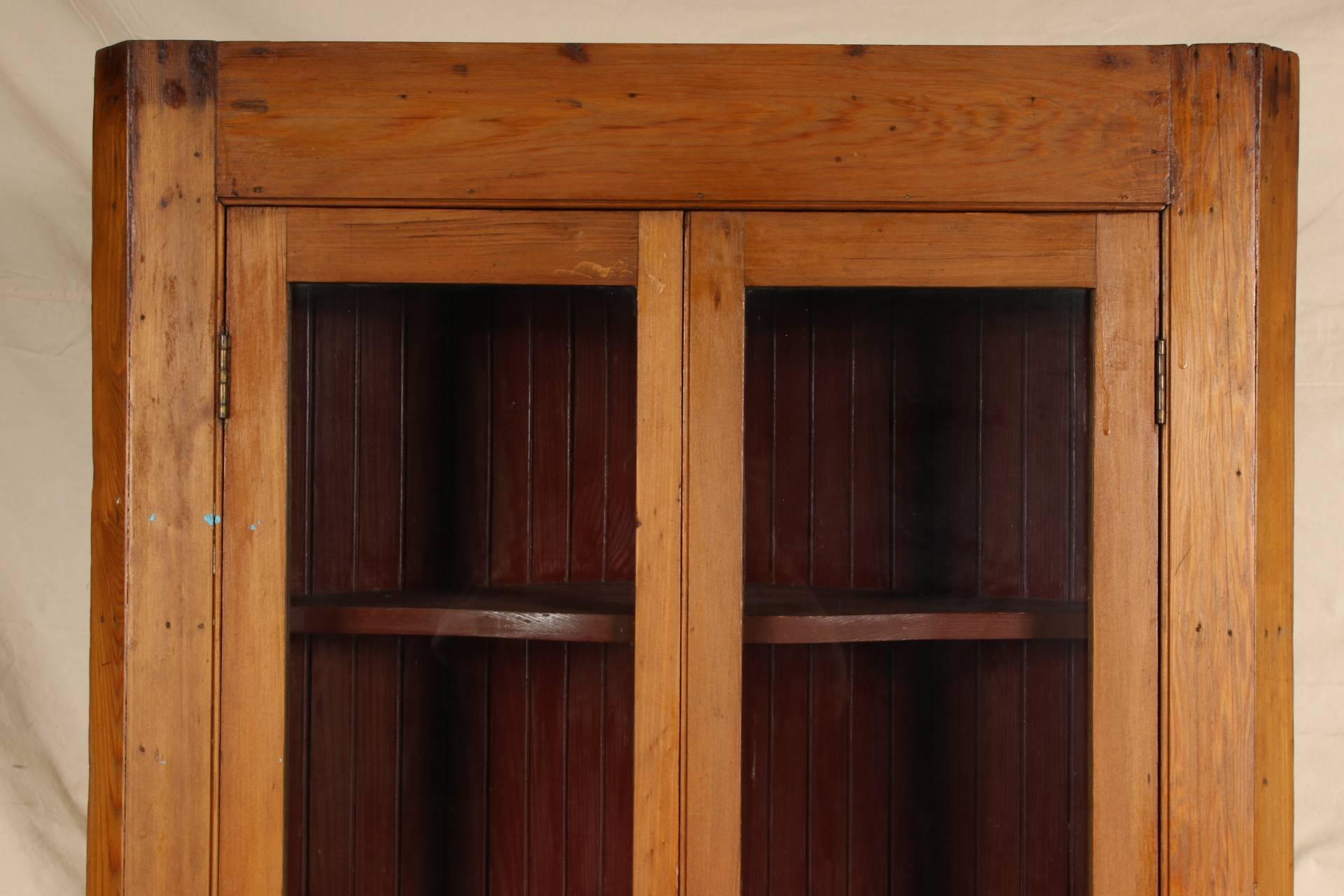 Two-part, the top cabinet with canted corners and double glazed hinged doors with a brass latch. The interior constructed of vertical planks with three shaped shelves all in barn red paint. Mounted on a lower cabinet with carved recessed double