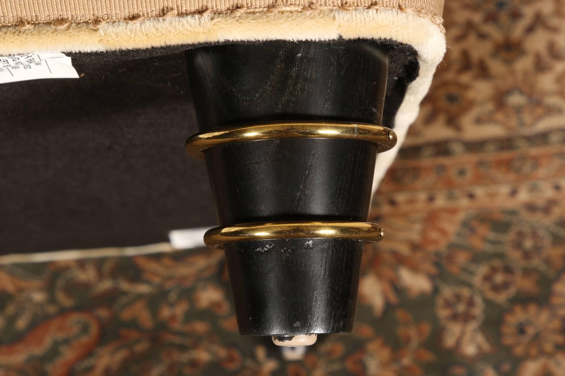 Square shape, upholstered in striped tan velvet with a center button. The lower frame edged in tan grosgrain, raised on ebonized cylindrical legs with brass rings. In very good condition.