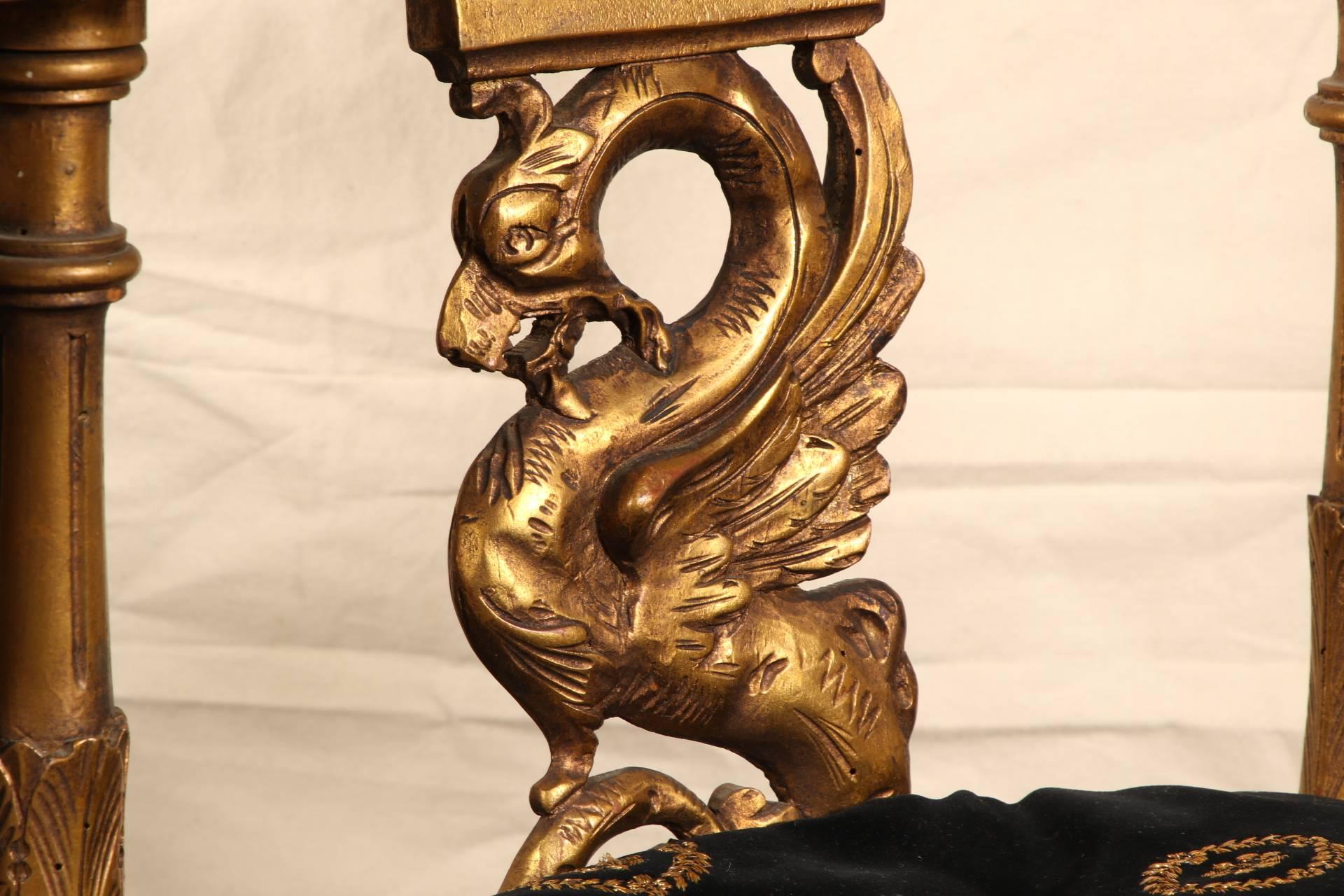 Empire style elaborately carved with foliate scrolled top rails and aprons, winged griffin supports at the backs, and putto masks on the crest rails. The triangular seats raised on fluted legs with turned stretchers and tiered turned feet.