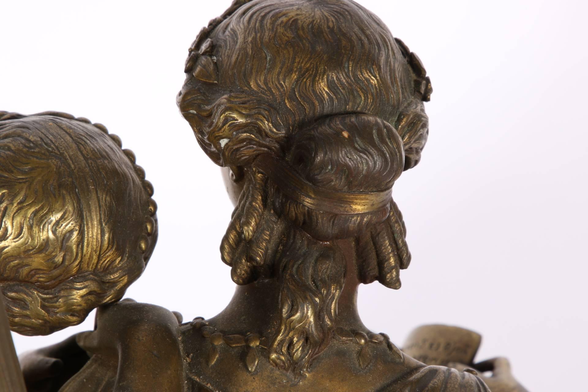 Cast bronze. A pair of neoclassical female figures dressed in heavy drapery and seated on a bench while pouring over a book. Mounted on a black painted metal base. Marked 16141 on the lower left back of the bronze. With attached lamp standard.