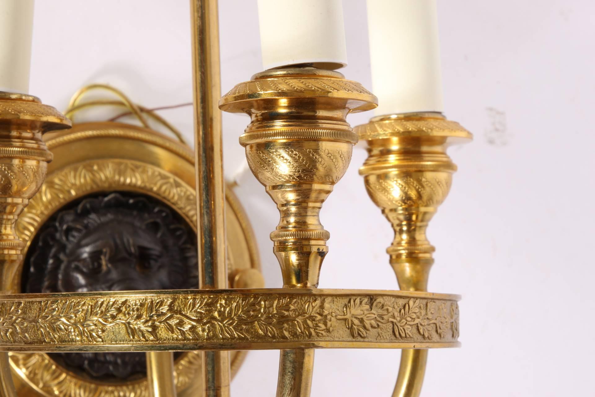 Made in Italy. Three candle socket lights each on a leafy decorated circular frame attached to a leafy roundel with a cast dark metal lion mask support. Artichoke terminals and black tole shades with gilt neoclassical motifs. Four of the six white