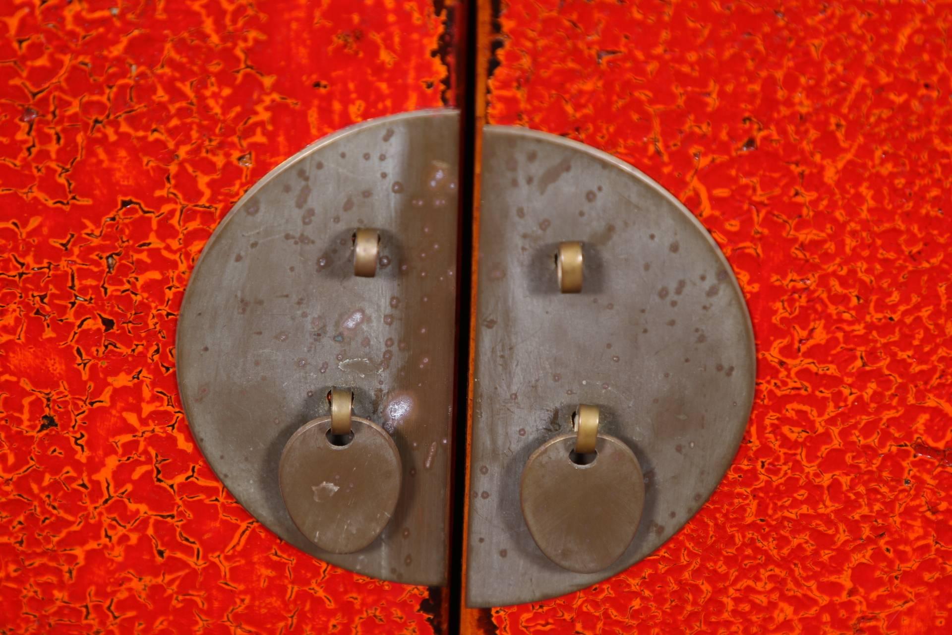 Rectangular wood cabinets in a mottled red lacquer with intentional worn looking edges overall and lacquered inset wicker tops. Single apron drawers overs double doors, all with gray metal hardware (lacking the door lock bolts). Shaped lower frames