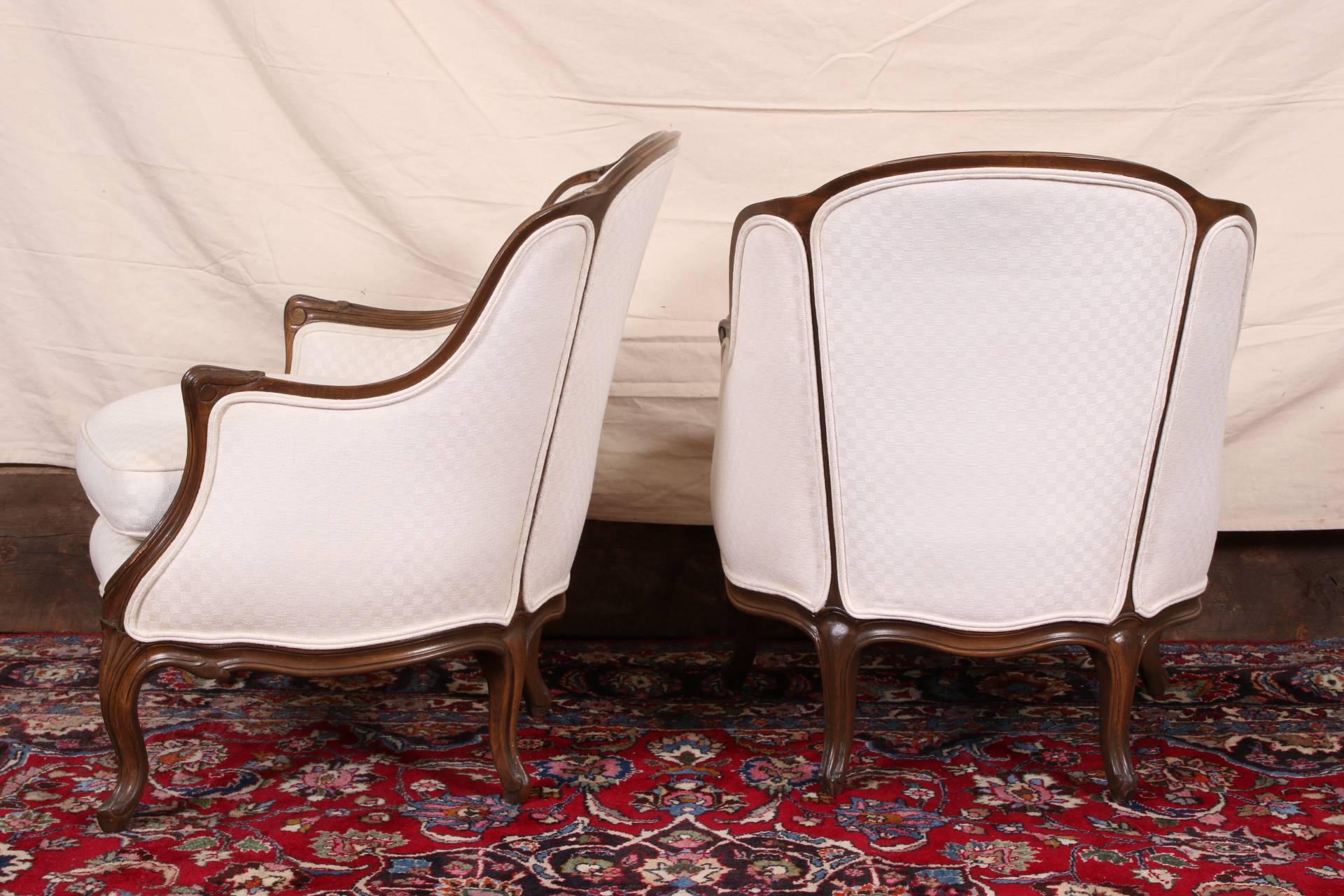 Carved walnut frames with scrolled arms and acanthus leaves on cabriole legs. Upholstered in a cream checked fabric. 
Condition: some wear to the finish on the arms and very slight markings to the fabric.