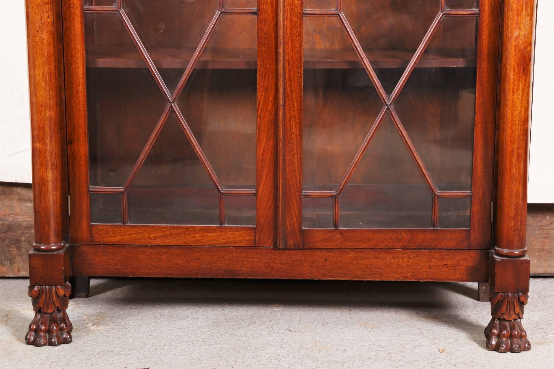 The top frame with two short drawers with glass pulls over twin column supports for the double glass mullioned doors with brass keyhole and a key. The cabinet is raised on carved lion's paw and acanthus leaf feet in front and square feet at the