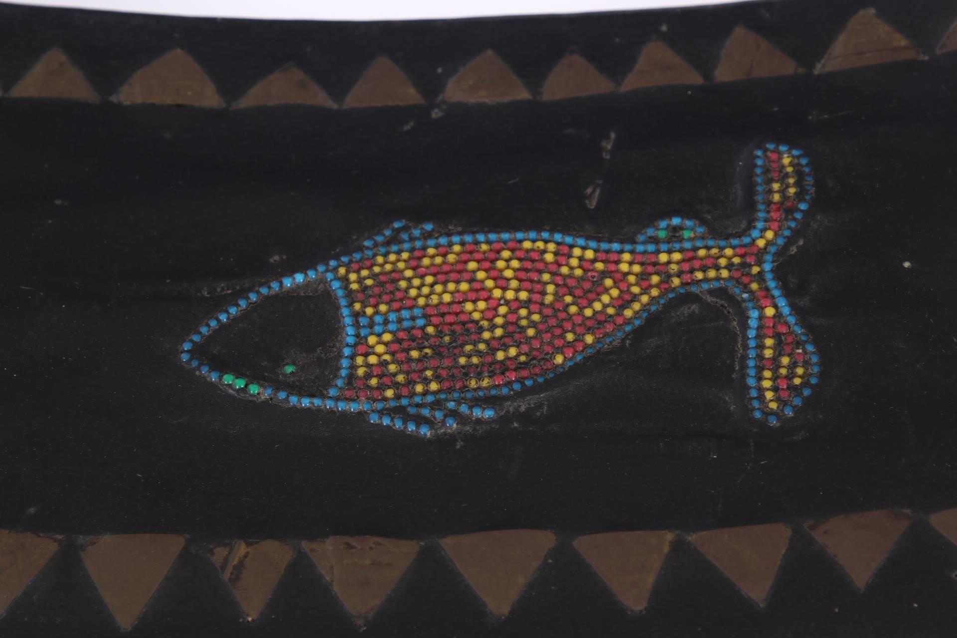 In dark brown paint with a rectangular base and shaped and carved support. The curved seat with brass triangular inlays on all sides an a glass beaded fish in the center. 
Condition: worn corners top and bottom, a few losses to the fish fins,