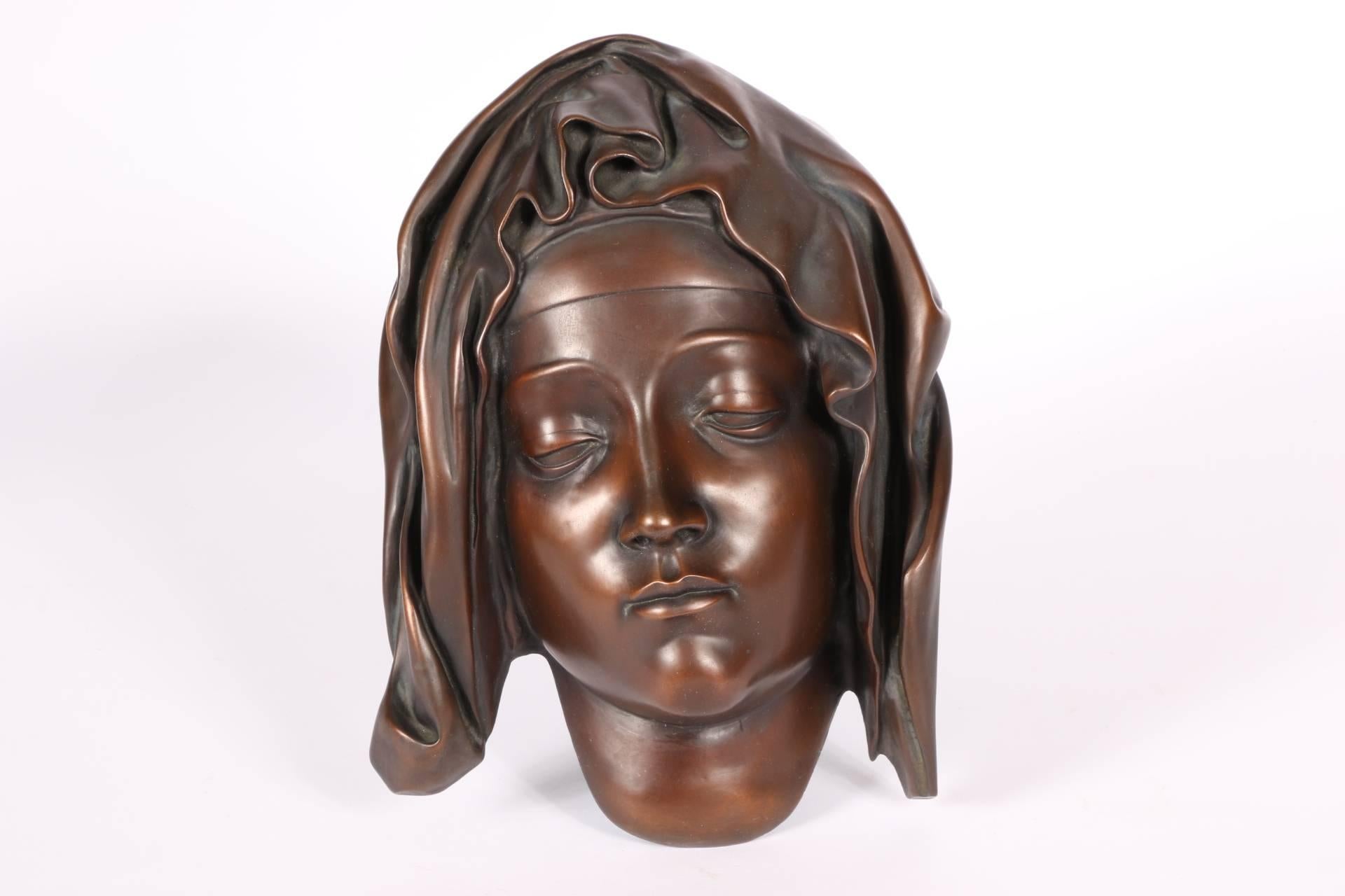 Hollow cast bronze in a red/brown finish. The Virgin with a somber expression, wearing a head scarf with elaborate folds. Reminiscent of Mary in the marble group of the Pieta in the Vatican, Rome. With loops and wire for suspension on the back.