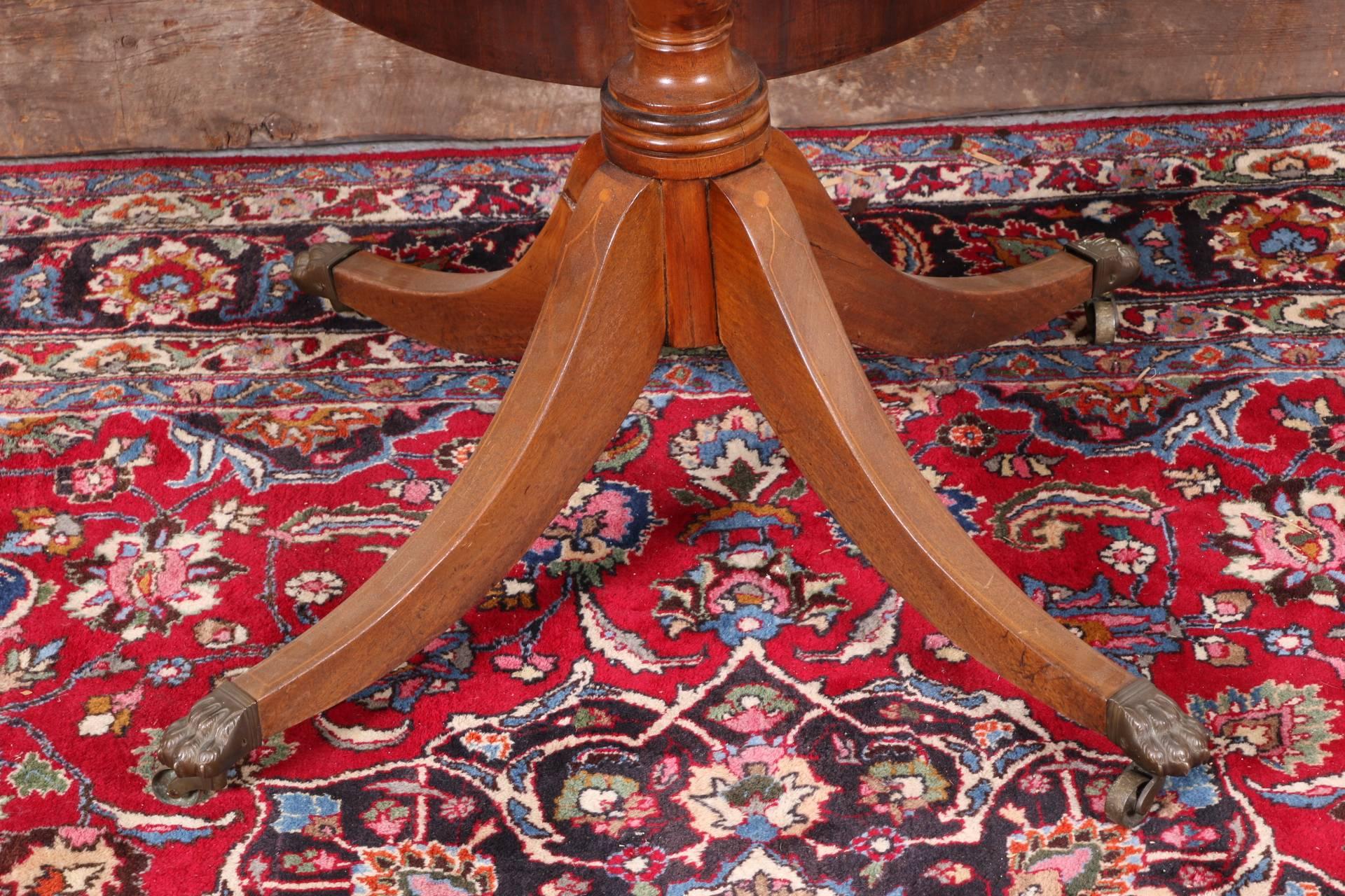 The oval top with inlaid burled cross-banding, and a baluster support on four splayed legs ending in brass lion's paw feet and casters. 
Condition: water damage to inlaid cross-banding, some scratches and dings to the top