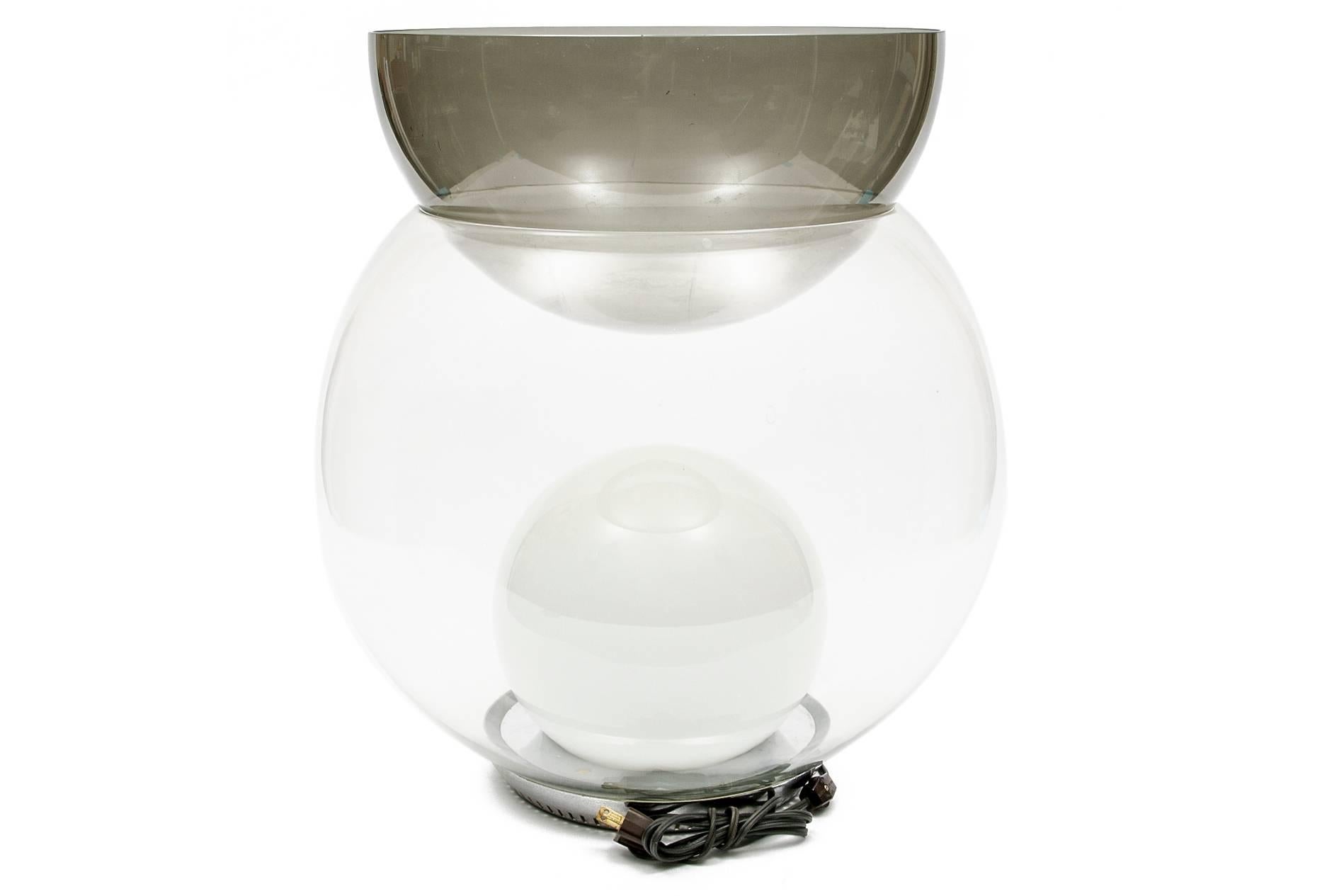 White glass orb lamp within a large clear top quality thick glass globe form having a smoky glass jardinière top. Pierced chrome base.
Condition: no chips or losses. The upper smoked glass bowl has white residue or etching, possibly caused from