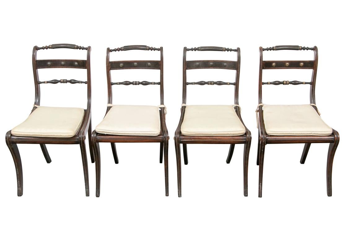 For restoration. Delicate and refined set of four particularly handsome Regency chairs with crest rails turned on the ends, scrolled sides and double back supports. One back support flat with brass bosses above a turned support bar with brass rings.