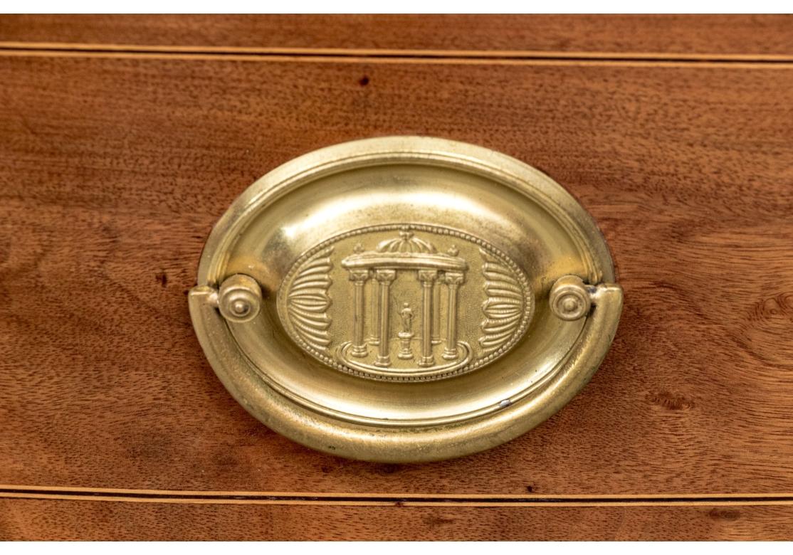 The fine chest with four graduated drawers each with fine string inlay and with a pair of brass oval bales decorated with a classical columned rotunda and brass key holes. All drawers are lined in a striped fabric and the top drawer has