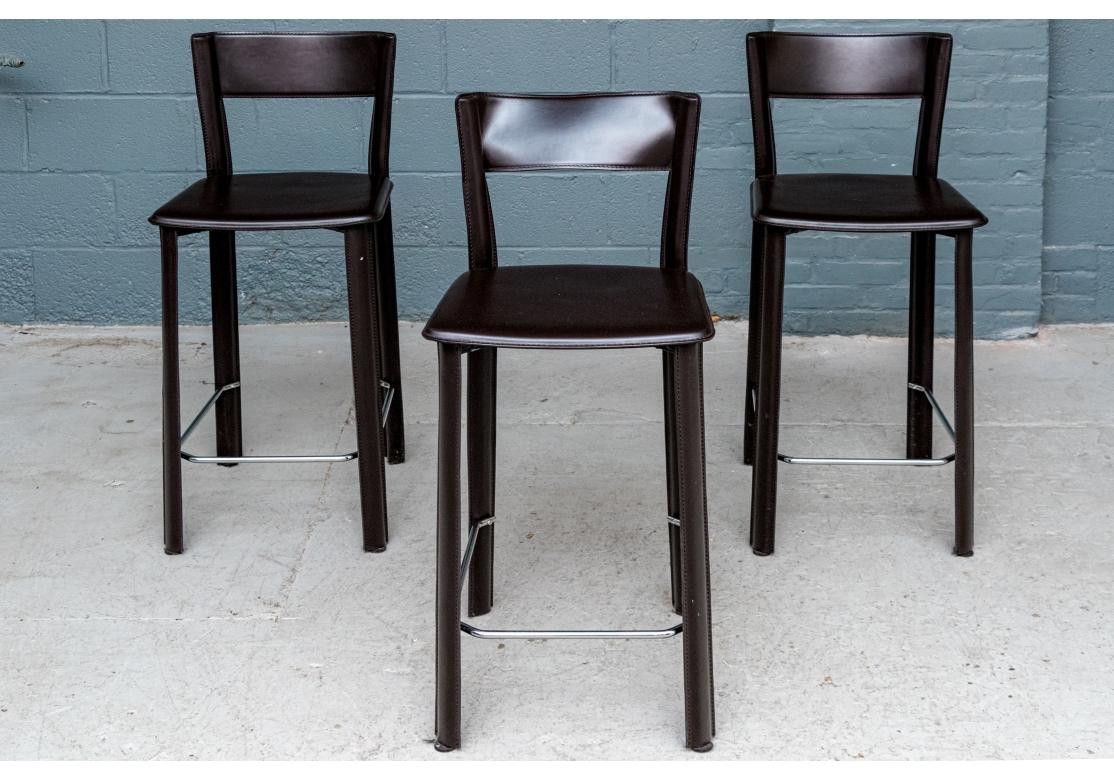 Set of three brown leather counter stools by Frag with slung back rest, seats with top-stitching details, three-sided chrome stretcher/footrest. Made in Italy.

Dimensions: 16 1/4