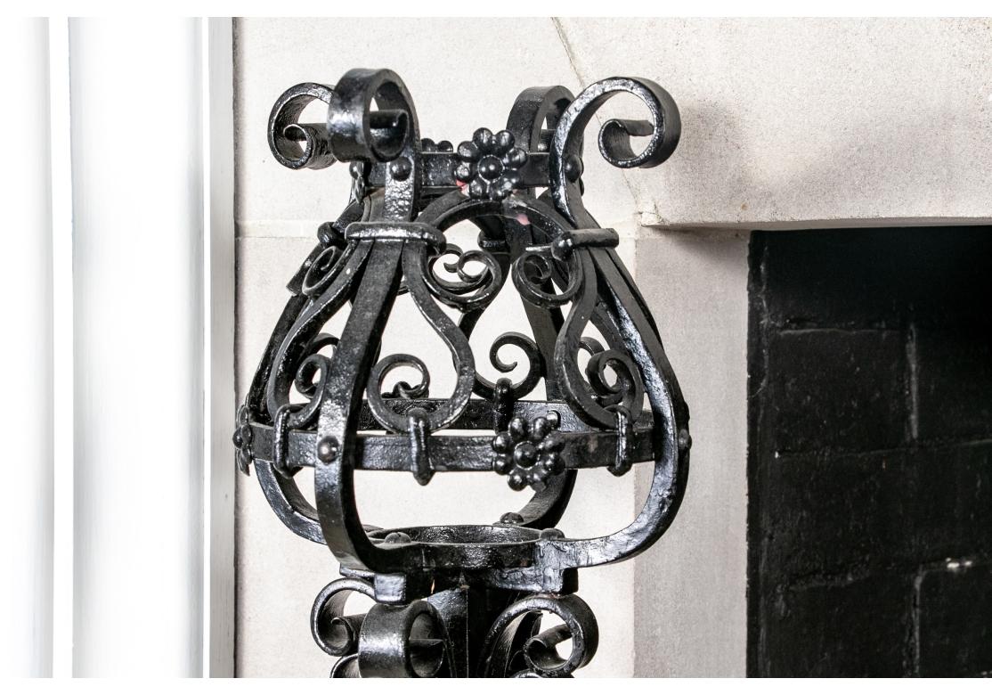 Elaborated crafted set of andirons, fire tools and log holder. Pair of large intricately scrolled and pierced andirons each in a black-painted finish. The tops each garnished with a spherical globe that also doubles as a candle holder. Accompanied
