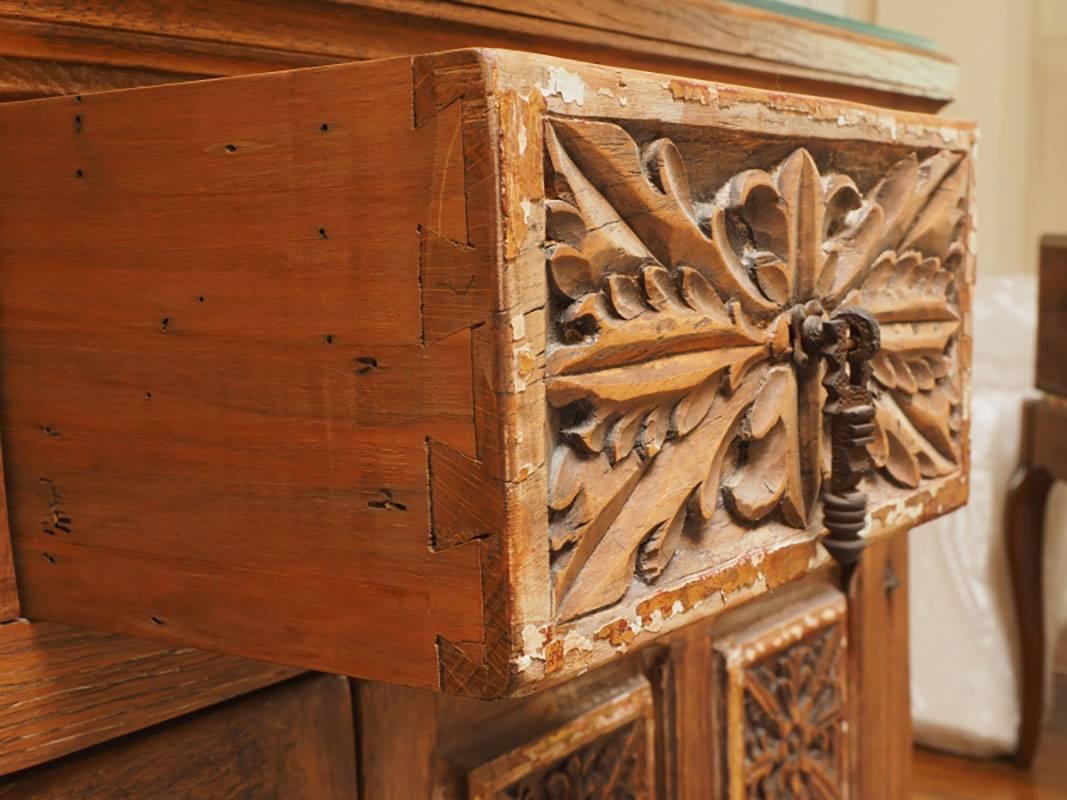 Features carved and gessoed panels, three top drawers, a two-door cabinet and wrought iron hardware. Distress and loss to the gessoed panels, which gives the piece a lot of great old-world character. Split to the top surface.