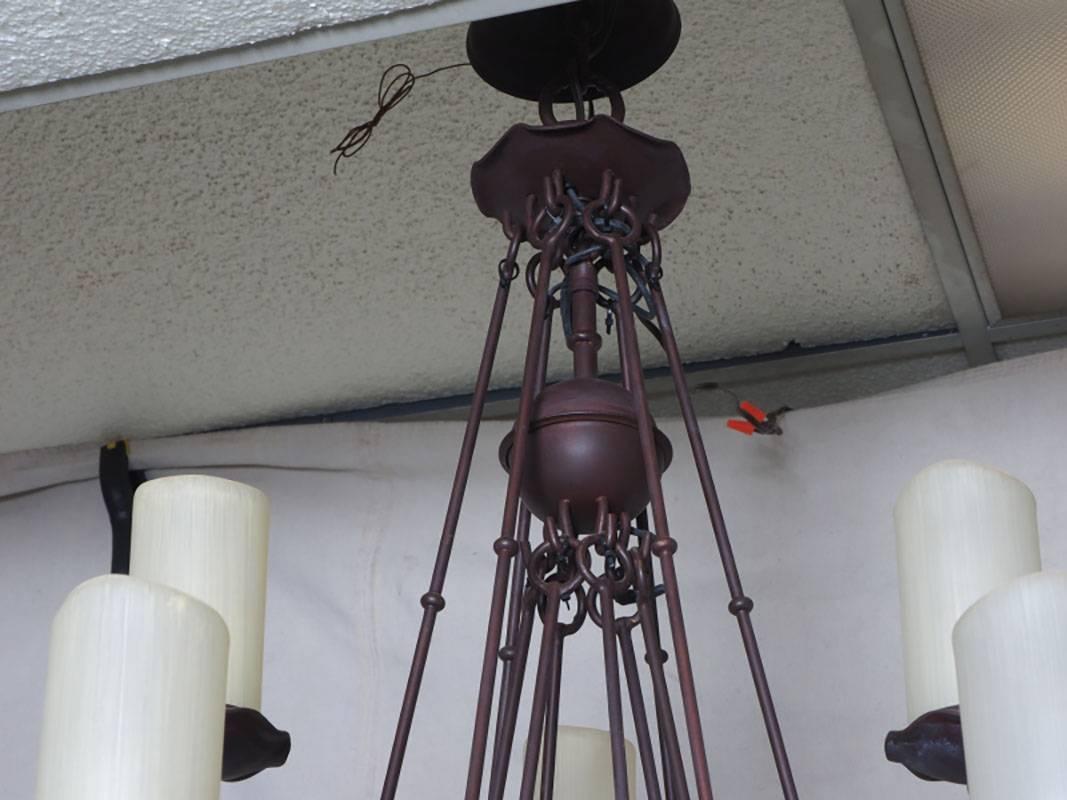 Wrought iron chandelier, three tiers with 21 arms and cylindrical frosted shades.
Each tier looped onto previous tier and suspended with long rods to top tier.
Bronze patinated finish in good condition. Ceiling cap included.