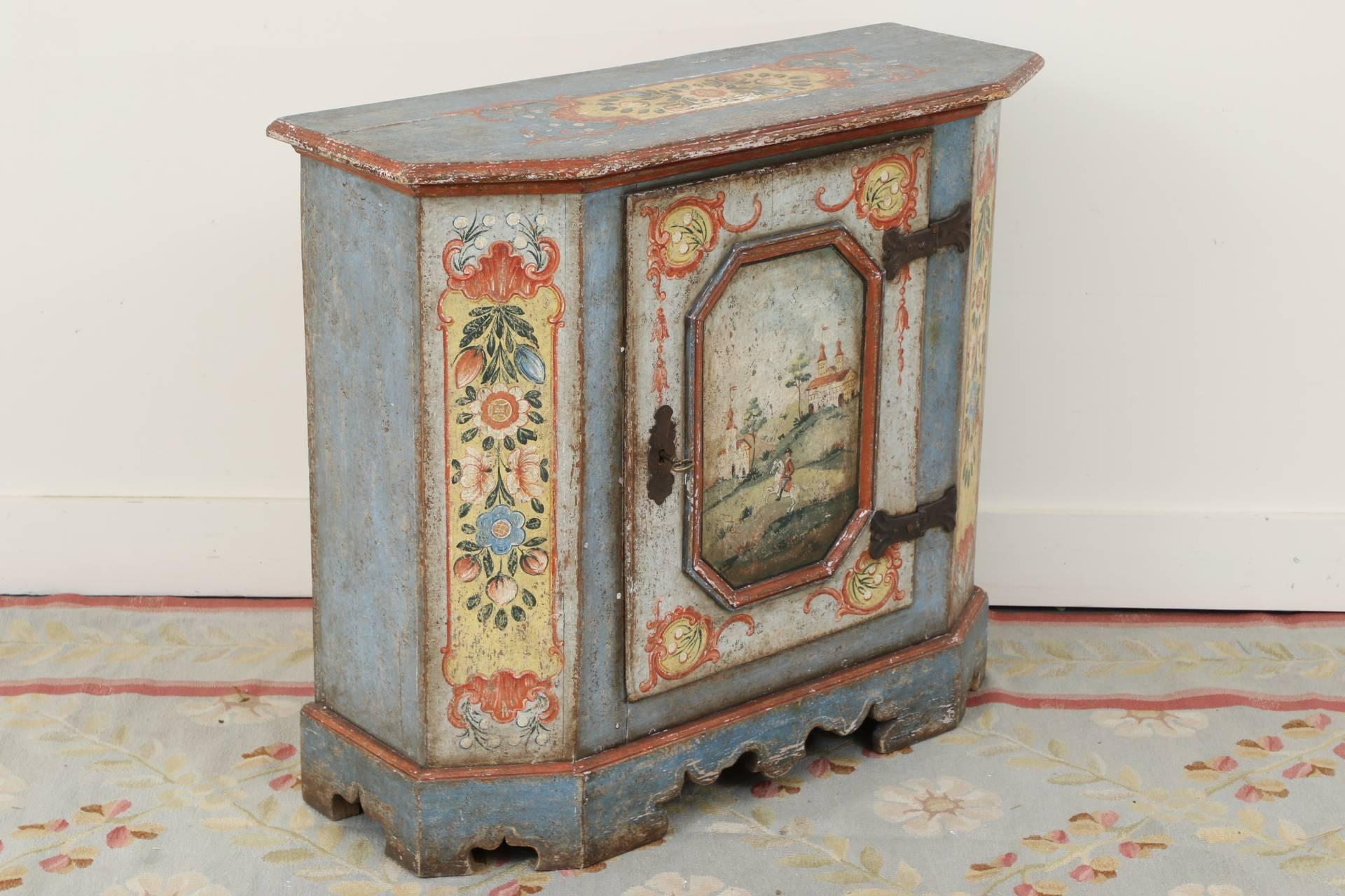 Rectangular with canted corners in blue paint with red edges. The top and front side panels with polychrome floral painted bands (perhaps painted later). The door with a centre angular panel decorated with a figure on horseback in a hilly landscape
