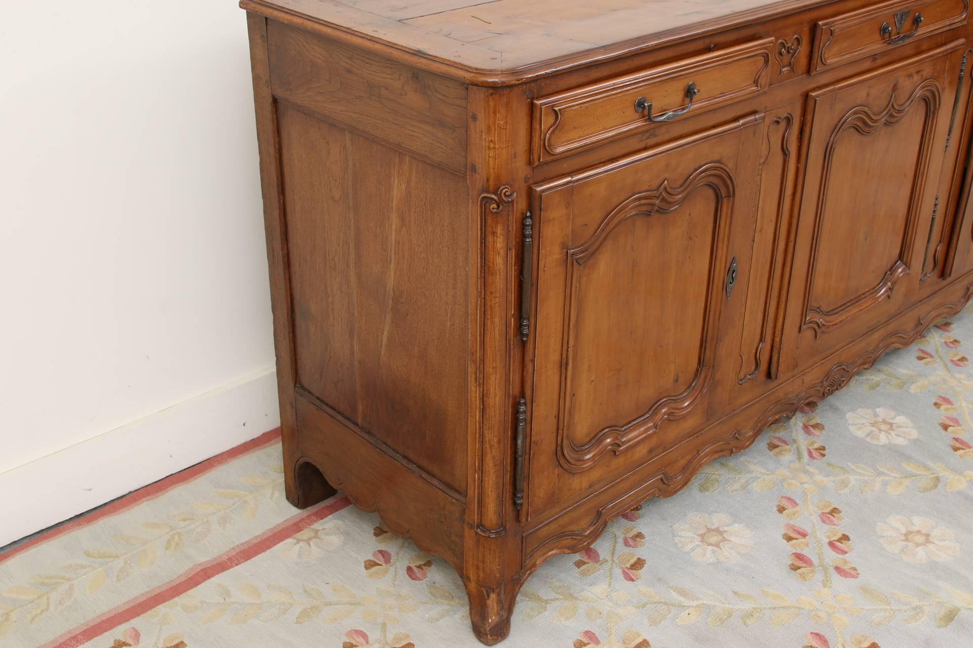 A tall sideboard (Enfilade) in walnut with carved and recessed panels on the front, and oak recessed side panels. The plank top with banded sides and bullnose edge, over three apron drawers with metal handle pulls (the enter one with escutcheon,