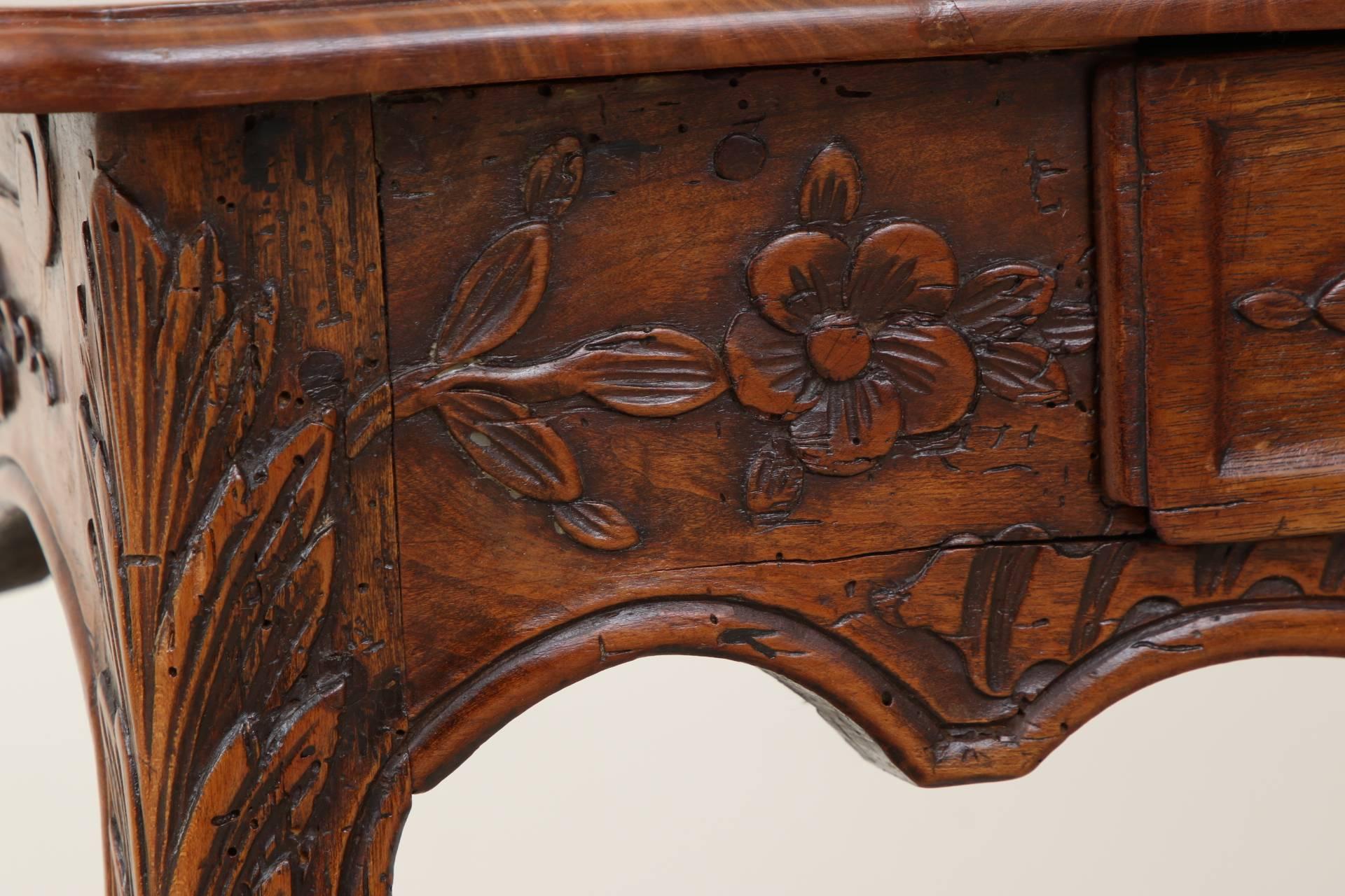 In fruitwood with a rectangular plank top and carved overhanging edge, circa 1750. A carved and shaped apron on all sides with floral and leafy bands and center shell motifs on three sides. A single apron drawer with a bronze knob pull. Raised on