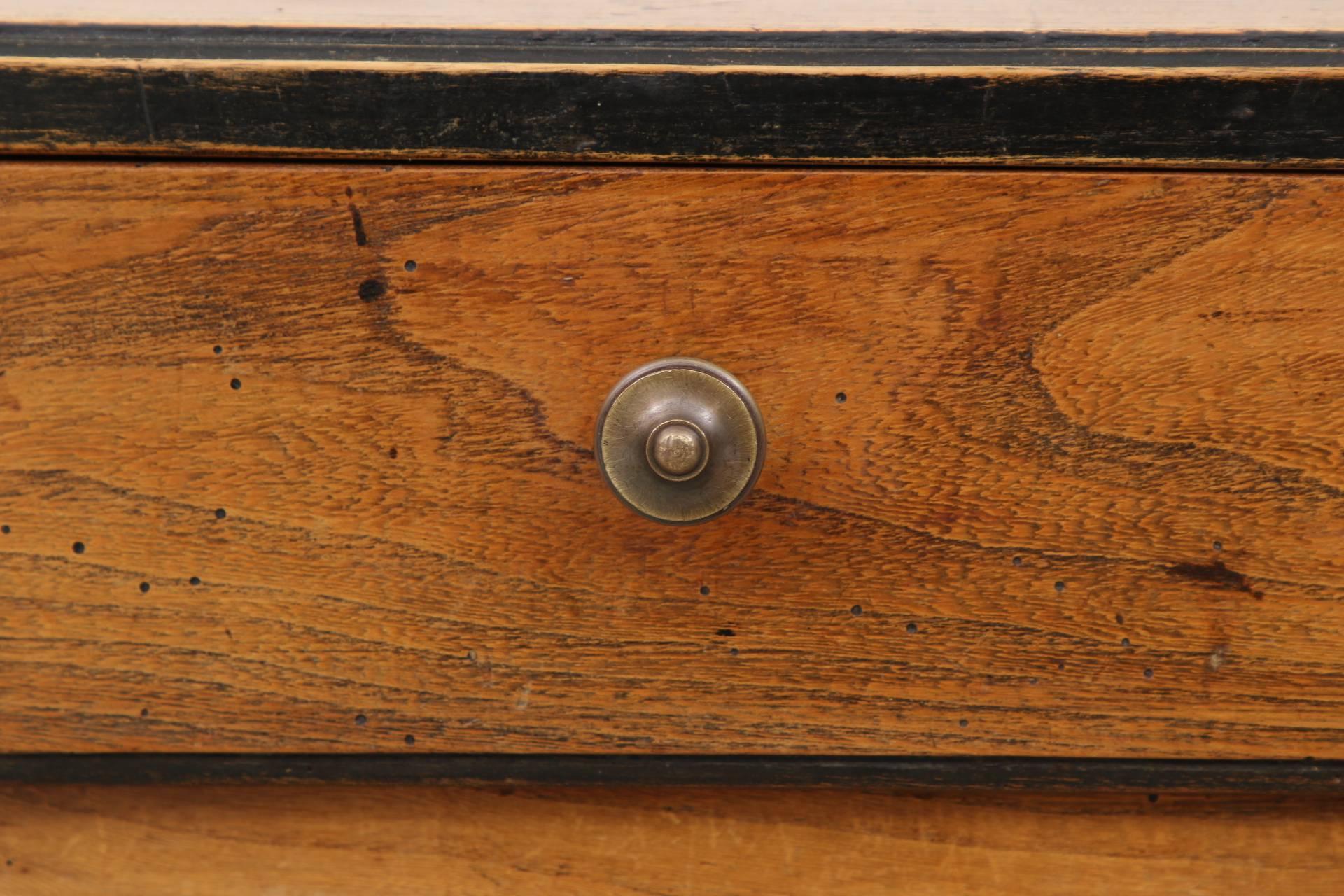 Carved in oak with a rectangular banded plank top with overhanging edge, over the apron with a single drawer with a bronze knob pull. Mortise and tenon construction for the elaborate turned legs on a shaped X-form stretcher with a turned finial.