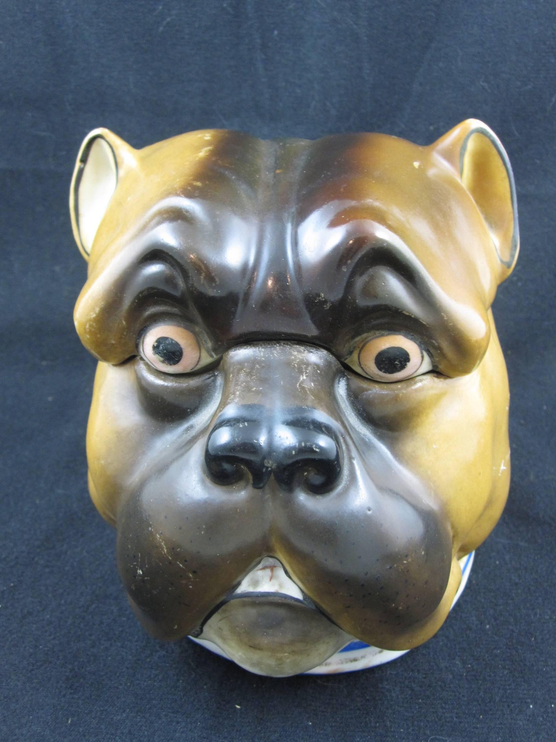 A porcelaneous lidded jar or humidor formed as the head of an English bull dog. Made in the Staffordshire region of England, mid- late 19th Century.

Modeled true to breed, realistic both in expression and coloring, a blue lined, buckled dog collar