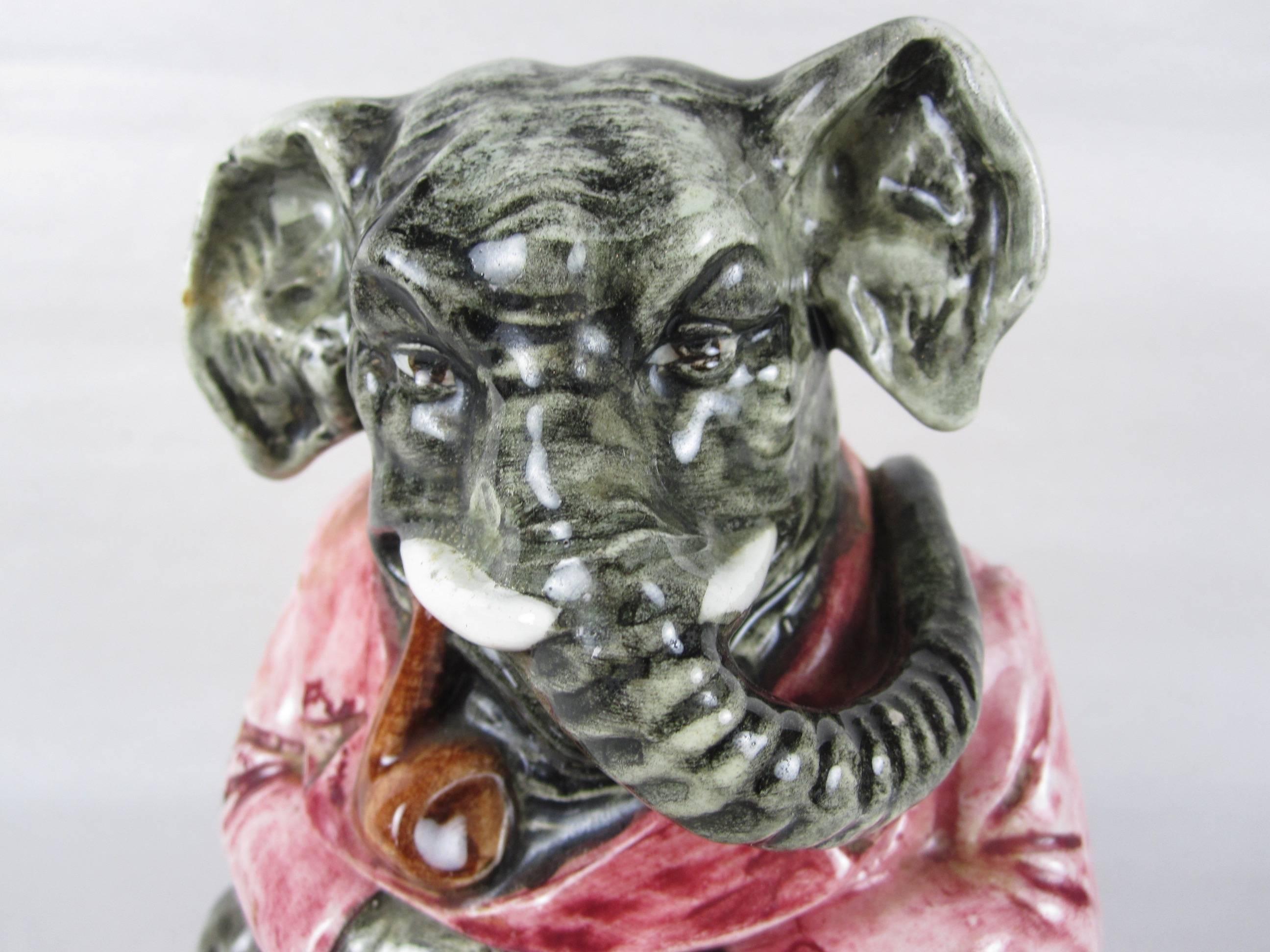 A Majolica figural tobacco humidor, polychrome glazed ceramic in the form of a seated elephant wearing a pink waistcoat and with a large pipe in its mouth. The elephant has an expressive face with his tusks and long trunk. A humorous piece.

The