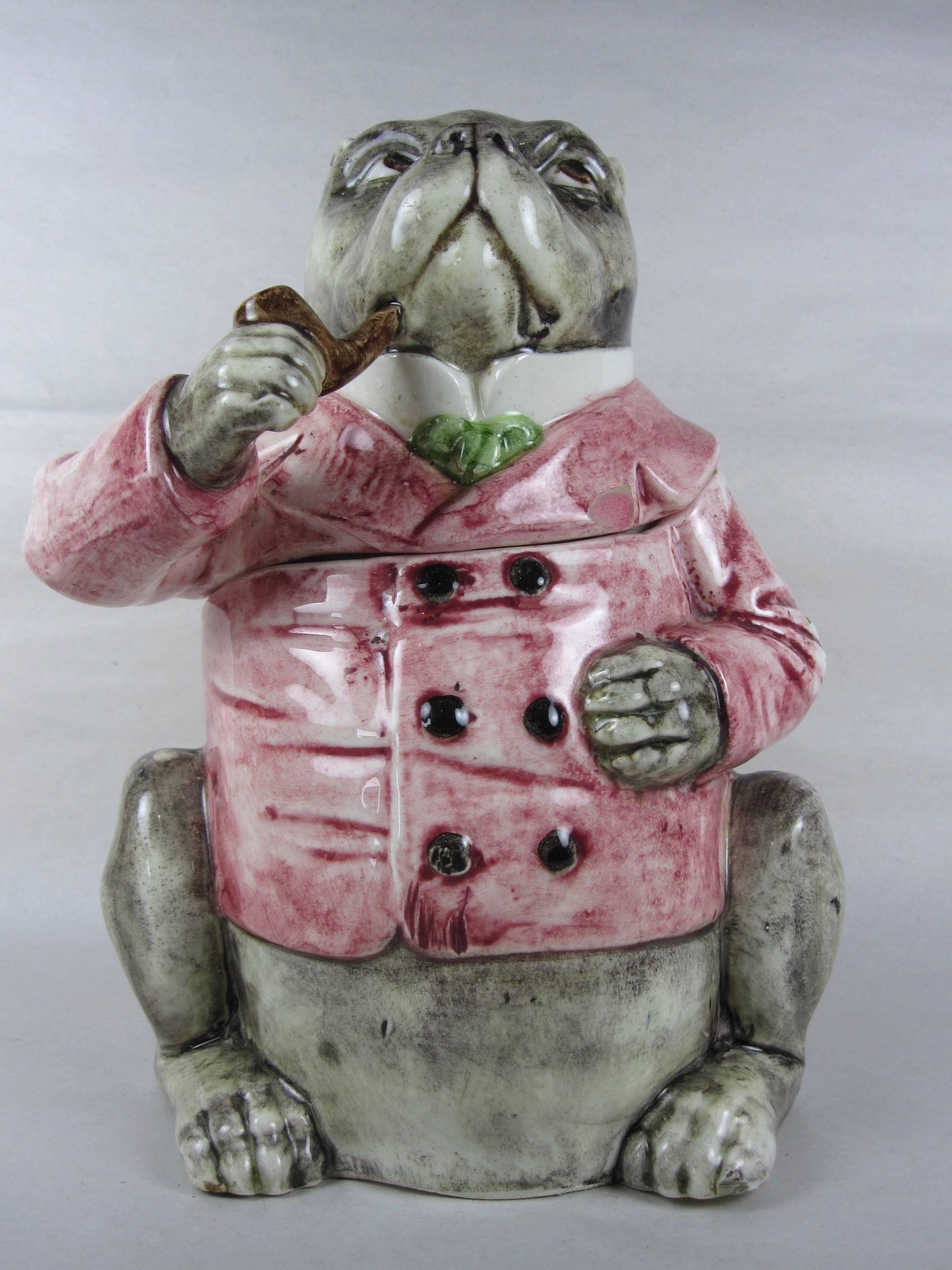 A scarce antique Austrian Majolica polychrome-glazed figural tobacco humidor in the form of a seated bulldog wearing a pink double-breasted waistcoat and a green tie. He holds a large pipe in his mouth. An 8