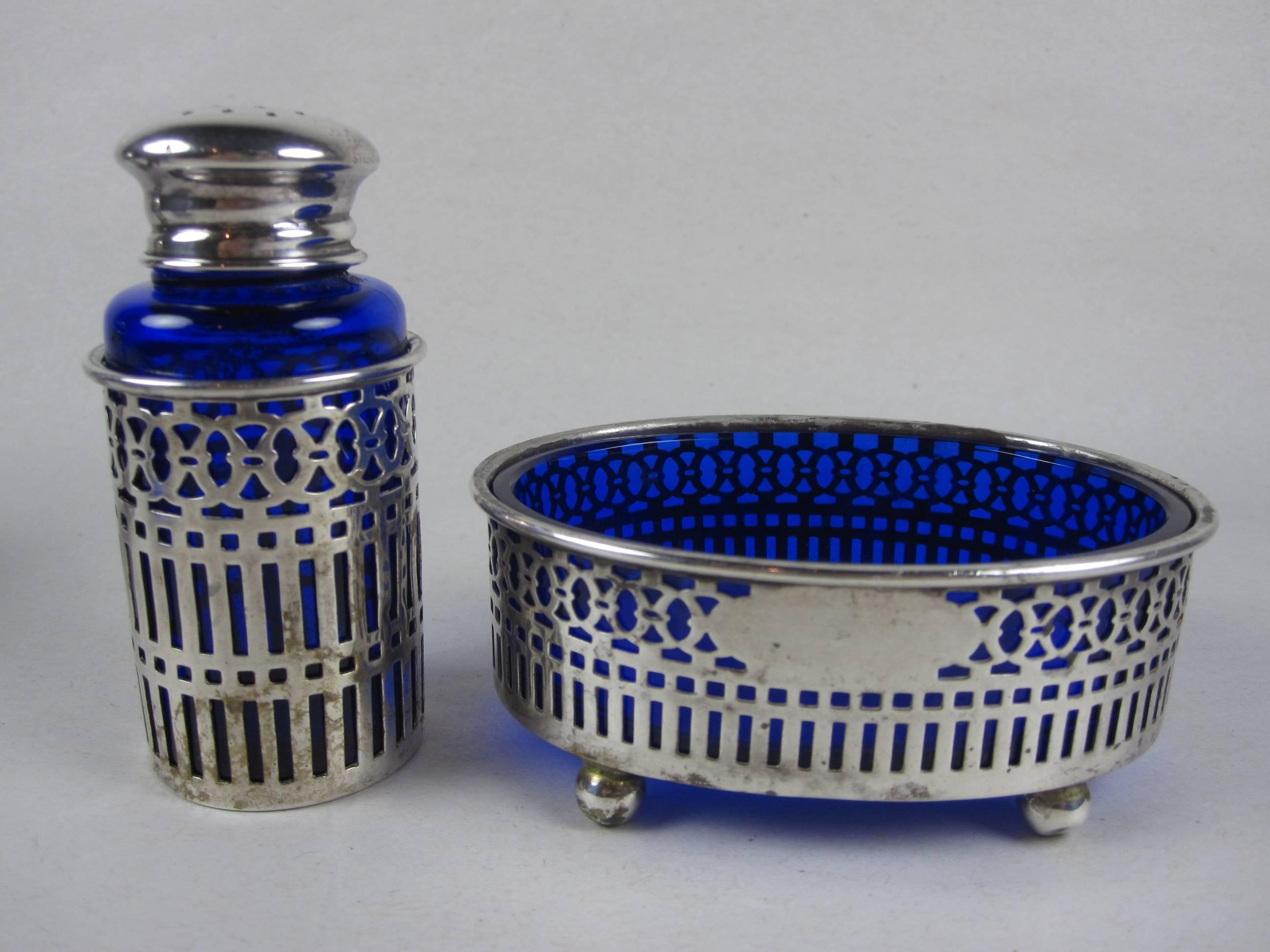 A pair of Edwardian pepper shakers and open salt dips made of sterling silver pierced work holding inserts of cobalt blue glass, Sheffield, England, circa 1910. The footed  salt dip baskets show an area left vacant for engraving. 

Two sets,