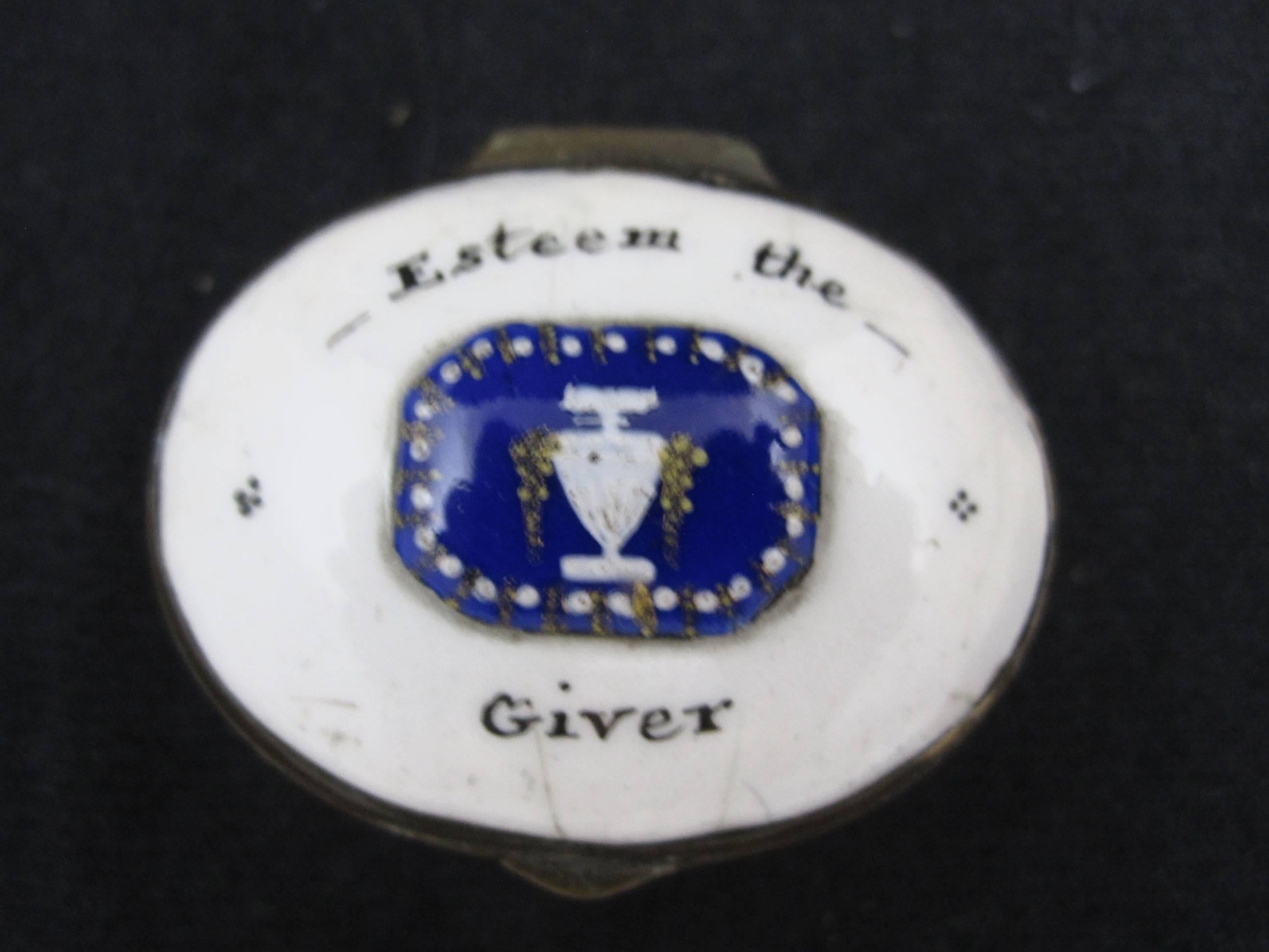 An 18th century English Bilston and Battersea snuff box, the motto reads, “Esteem the Giver.” 

A raised hand enameled cobalt blue shield with an urn, some gilding, the oval shaped box is copper framed. A silvered mirror to the interior lid. Still