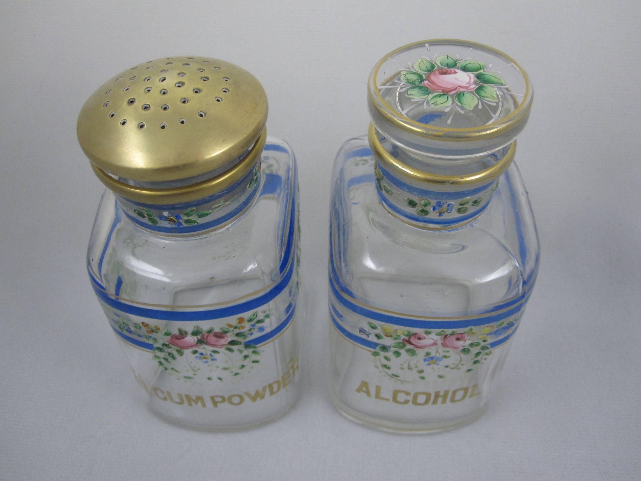 A charming pair of hand-enameled and gilded glass vanity bottles manufactured by the A.H. Heisey Company, Newark, Ohio, circa 1895.  

One marked Alcohol with a Rose topped glass stopper, the other marked Talcum Powder with a pierced brass Shaker