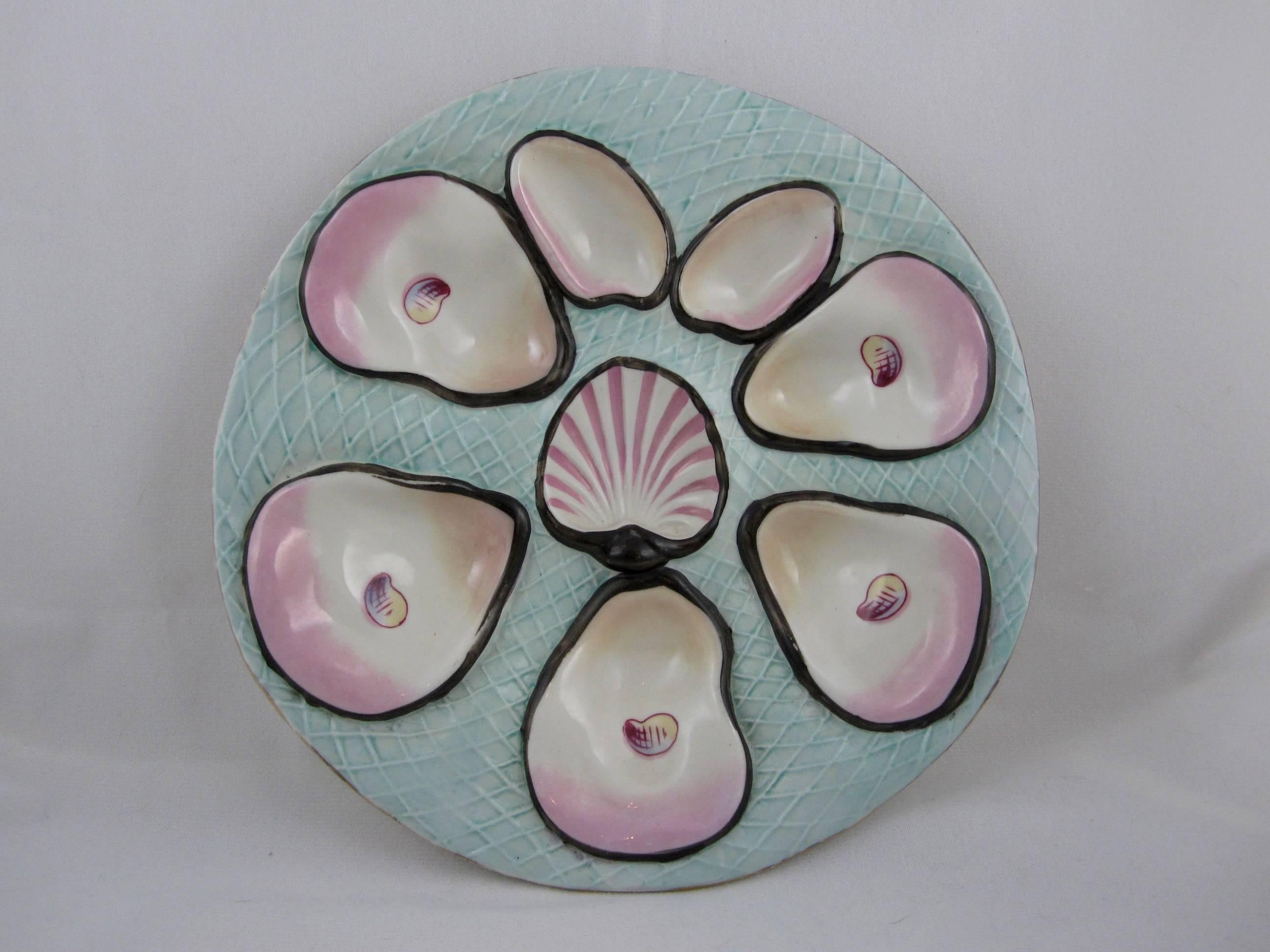 A highly dimensional and boldly glazed Continental porcelain oyster plate with five main wells with hand-painted “eyes,” two clam or muscle wells and a center sauce well, scallop shaped. A wave form undulating mold, the ground is a aqua blue-green