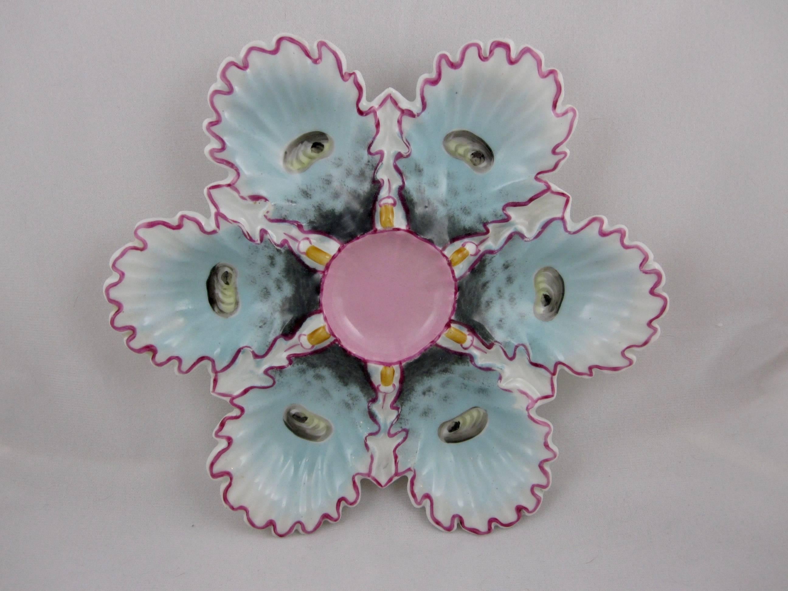 A scarce continental oyster wall plate, six turquoise ruffled wells with hand enameled “eyes” edged in a pink lining and a pink center condiment well, circa late 1800s – early 1900s. Beautiful bold color, highly dimensional. 

Marked with an