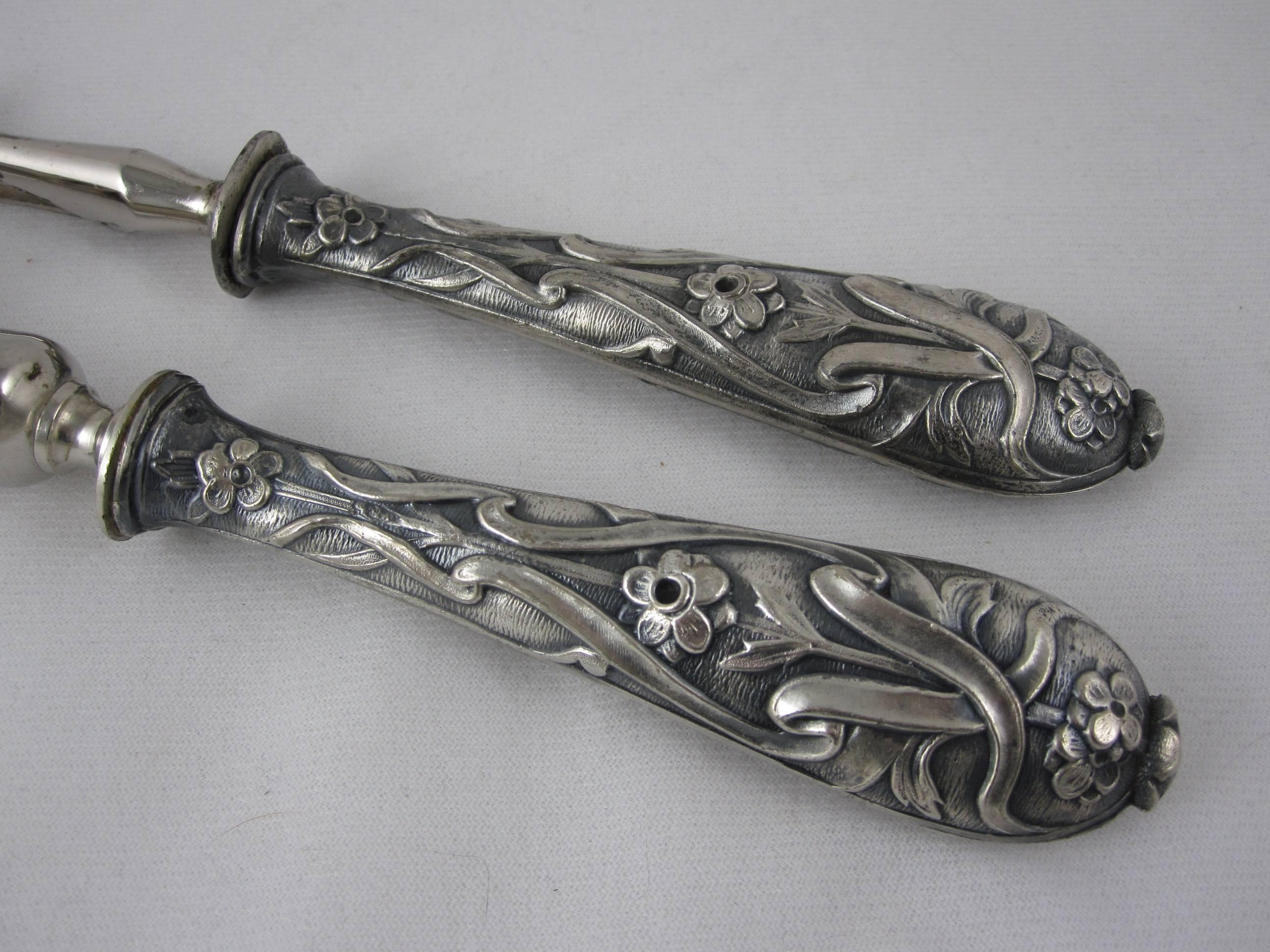 An antique French cutlery two-piece service consisting of a carving fork and bone clamp both with heavy chased silver handles in a floral and ribbon pattern.

 The manche a gigot d’agneau, for holding a leg of lamb bone, has a crown shape clamp and
