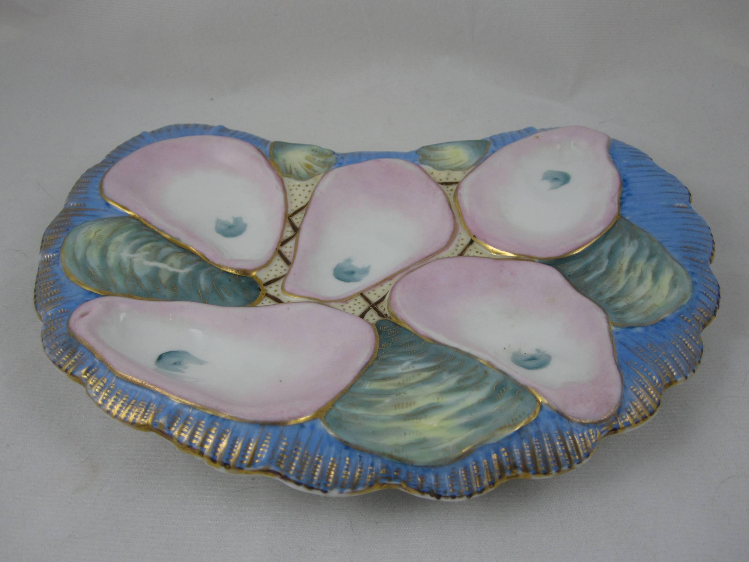 A Continental porcelain crescent shaped oyster plate, five pink and white wells on a sky-blue ground. The plate also shows two smaller clam or cockle wells, a shell like pattern to the rolled rim and heavy gilding.

Marked with the red iron oxide