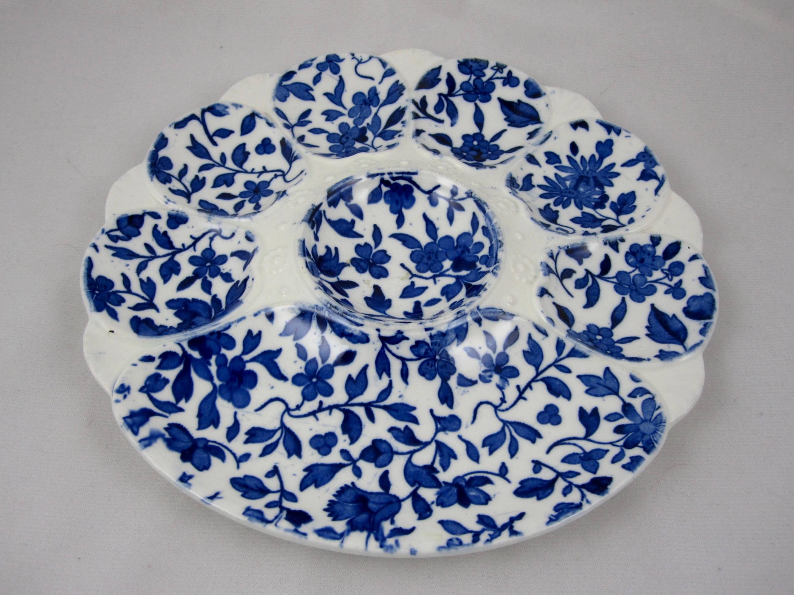 A flow blue transferware floral oyster plate, Minton, Stoke-On-Trent, England, mid-19th century. Six oyster wells and a larger cracker well surround a central condiment well ringed by the distinctive Minton mold work of raised dots and
