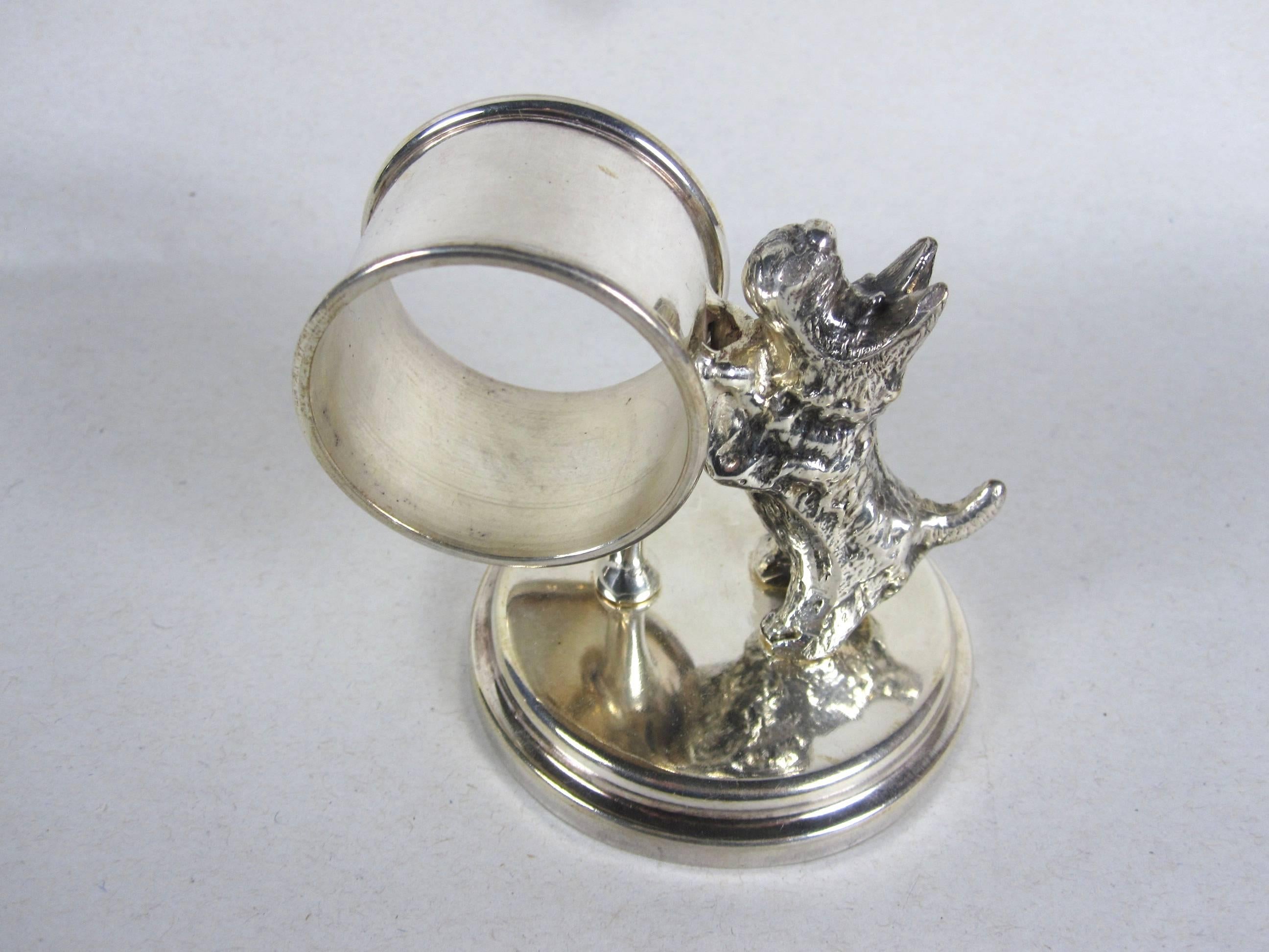 An antique Victorian Era Silver-plate standing napkin ring and place holder with a Scotty Dog rolling a barrel ring on a round rimmed base. 

Dating from 1890-1910. The dog and barrel stand are held in place with screws. Un-marked.

Heavy weight