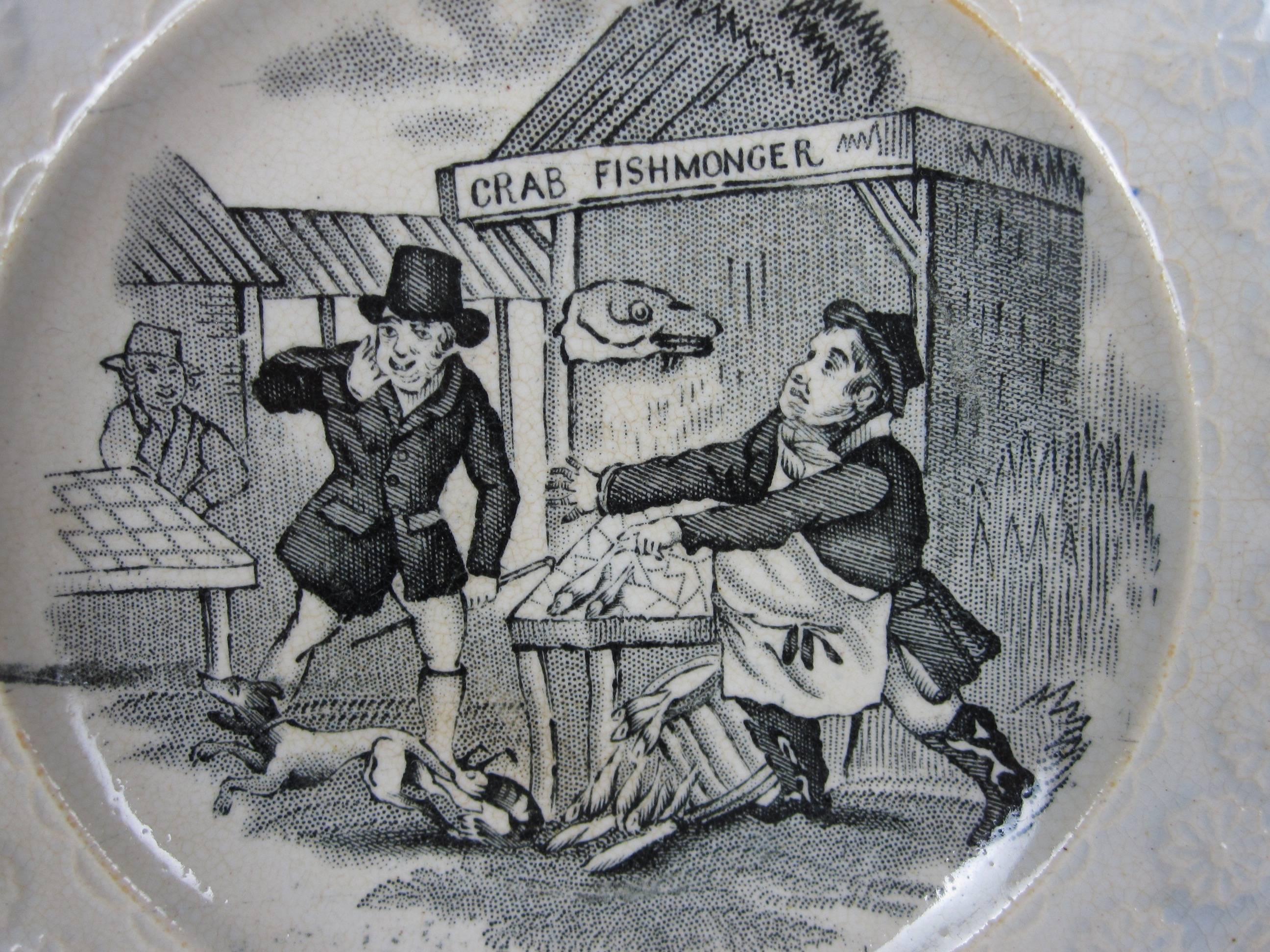 An antique English Staffordshire cup plate or child's plate, the pattern is titled “A Cheap Lobster.” The humorous transfer printed image shows a dog trying to escape a lobster that has bitten him, but the lobster holds on! The owner of the dog, who