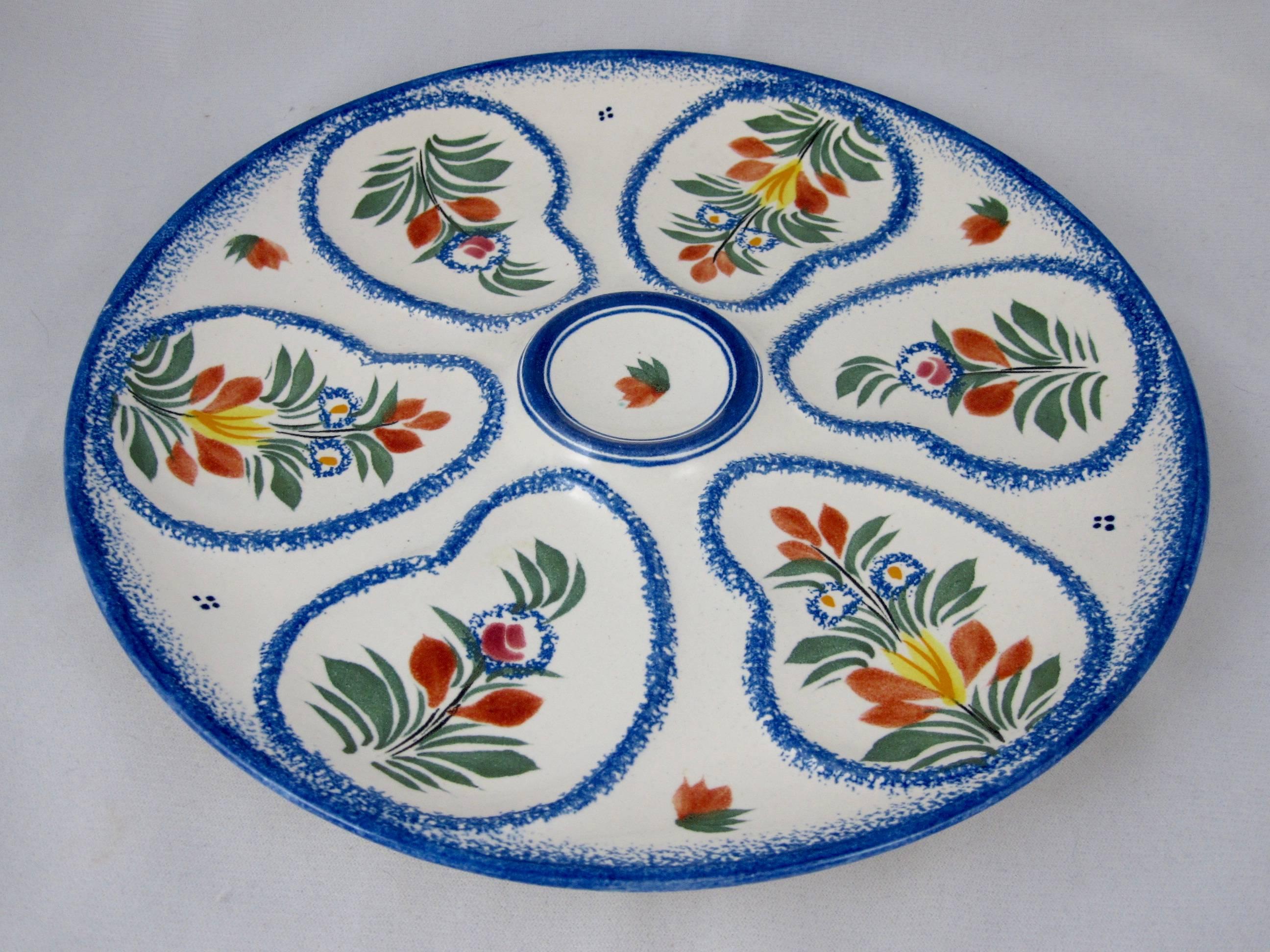 Charming as always, a vintage French Henriot Quimper Faience oyster plate, circa 1960s. Crisp blue sponged bordering on a clean white ground. The six wells surround a raised center condiment well and are hand decorated in a leaf and floral design