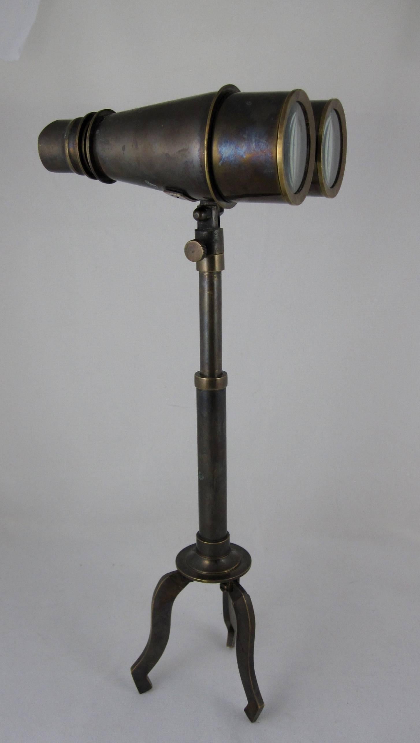 A vintage pair of tall field glass or maritime binoculars with a removable, folding tripod Stand. The glasses have fully adjustable lenses in very good working condition. The binoculars can be mounted onto a stand supported by a tri-footed base